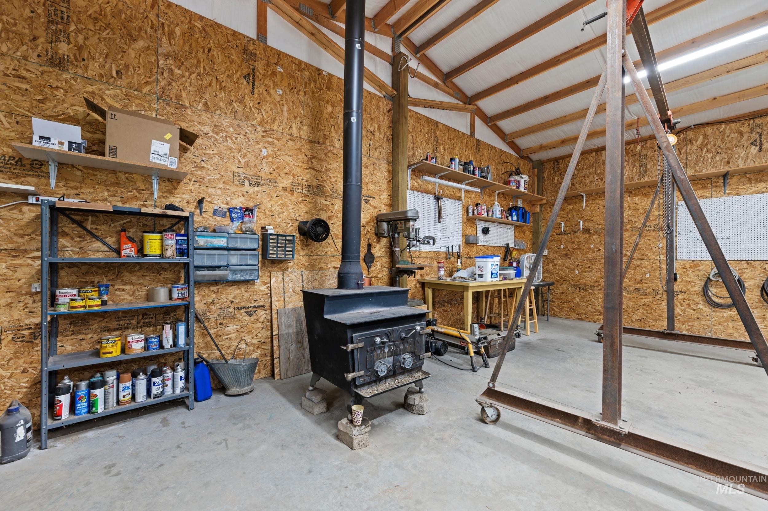 Miscellaneous room with concrete floors, a wood stove, a workshop area, and high vaulted ceiling