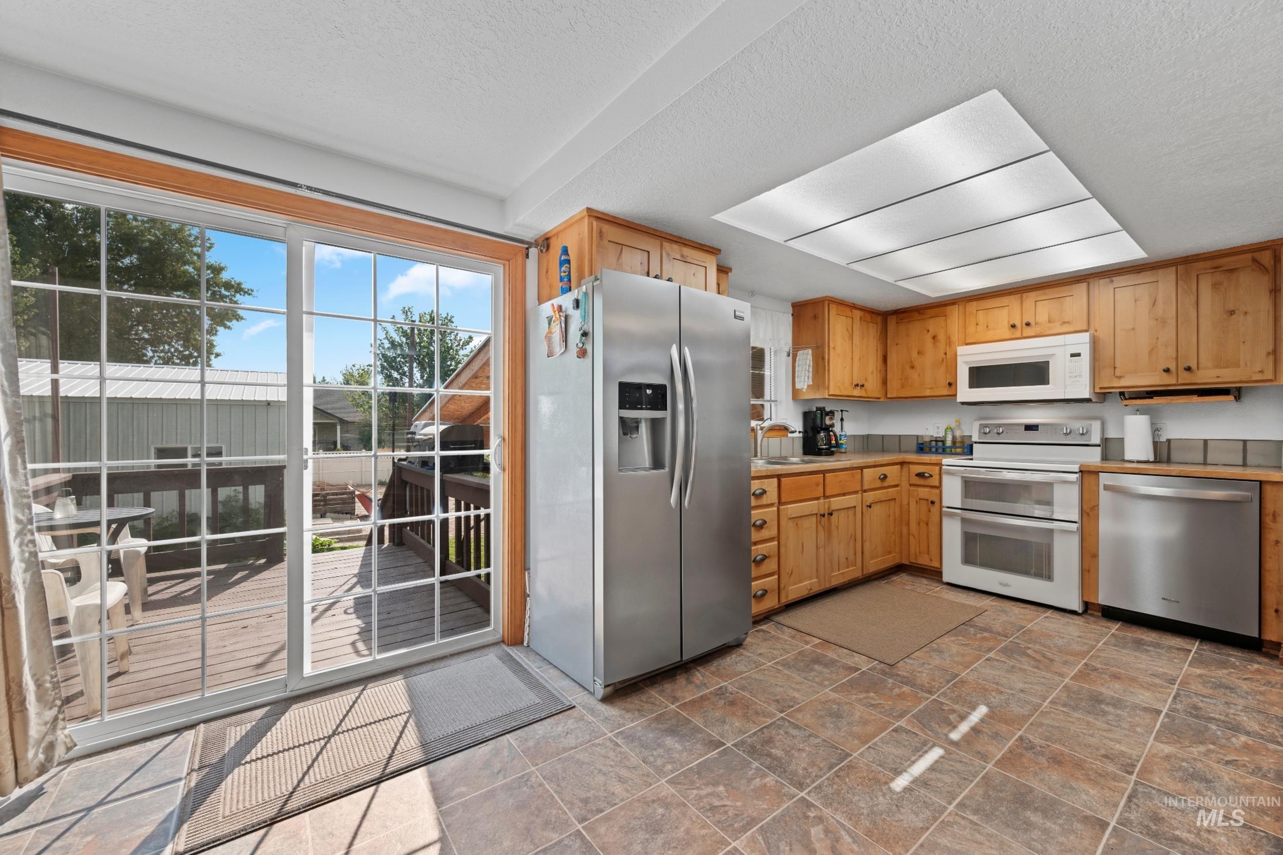 Kitchen with appliances with stainless steel finishes, stone finish floors, light countertops, and a textured ceiling