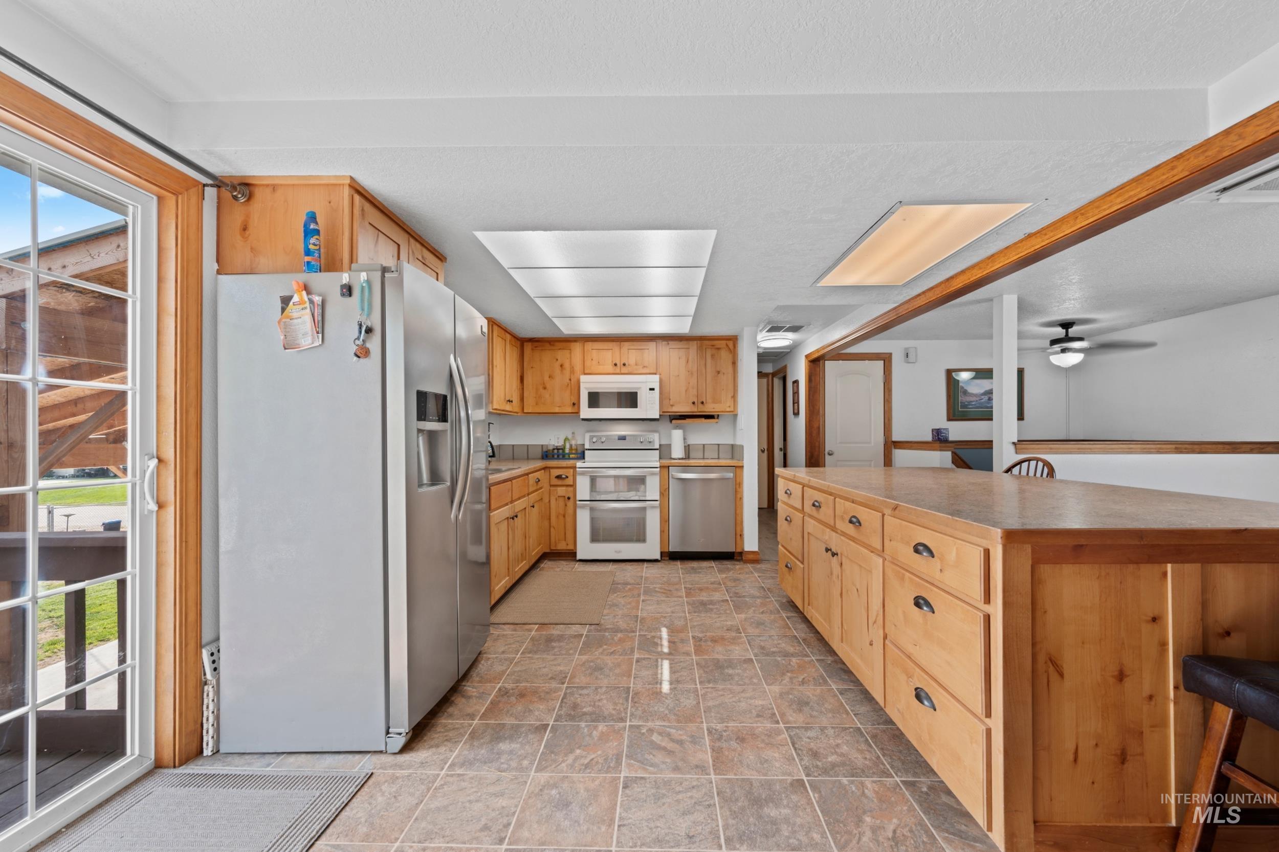 Kitchen with appliances with stainless steel finishes, a breakfast bar, ceiling fan, light stone finish floors, and a kitchen island
