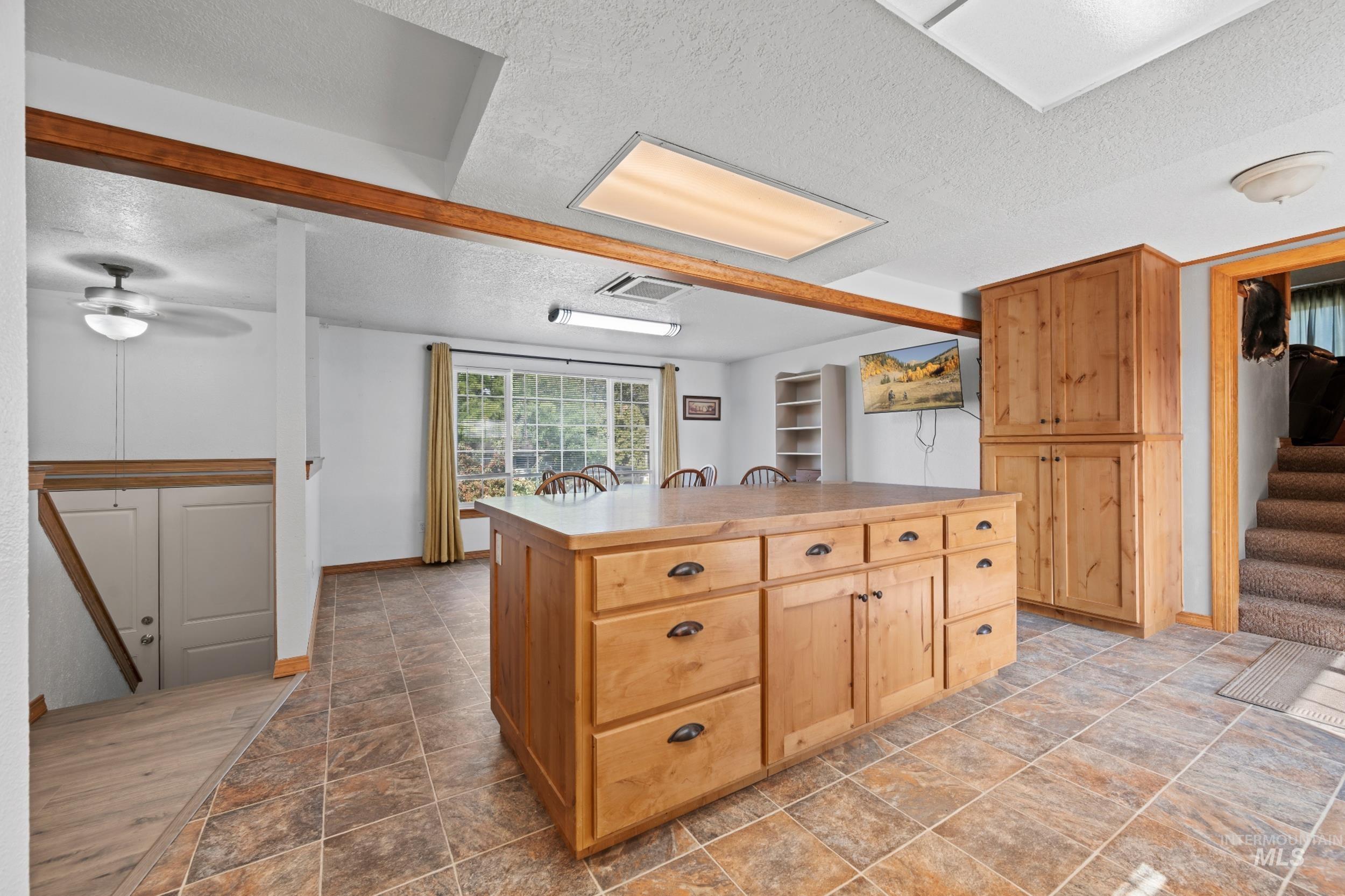 Kitchen featuring a textured ceiling, a kitchen island, light brown cabinetry, light countertops, and dark stone finish flooring