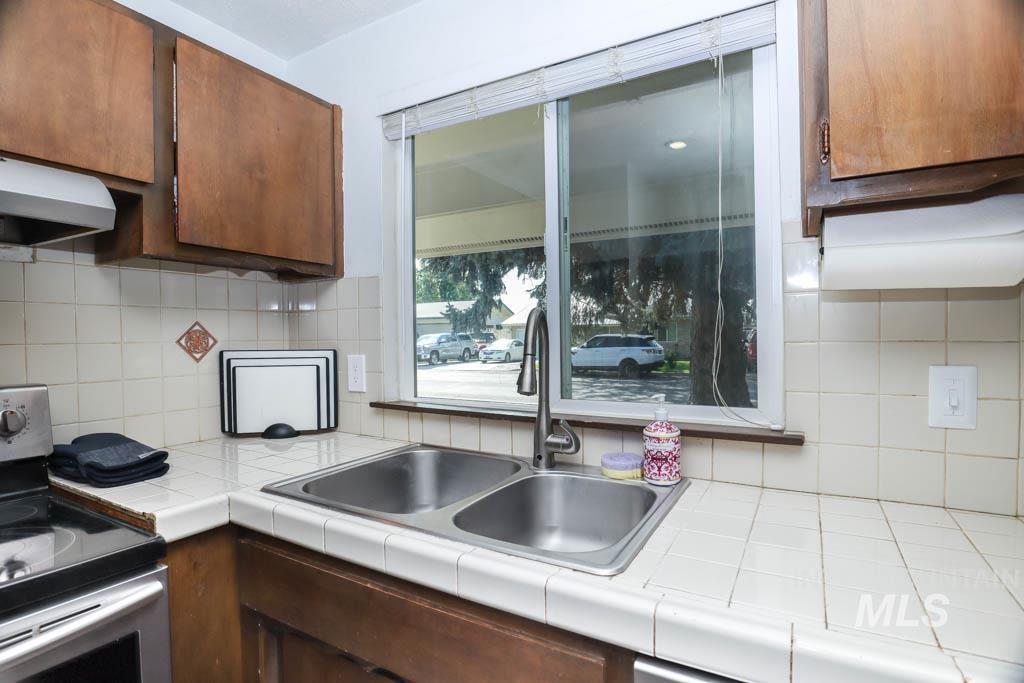 Kitchen with stainless steel range with electric cooktop, decorative backsplash, tile counters, under cabinet range hood, and brown cabinets
