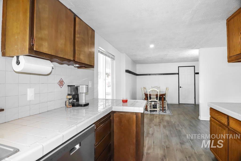 Kitchen featuring tile counters, dark wood-style floors, backsplash, dishwasher, and a peninsula