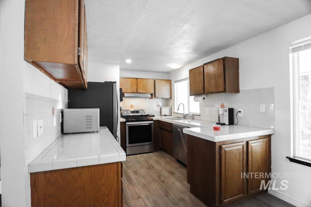 Kitchen with tile counters, appliances with stainless steel finishes, dark wood-type flooring, tasteful backsplash, and a textured ceiling