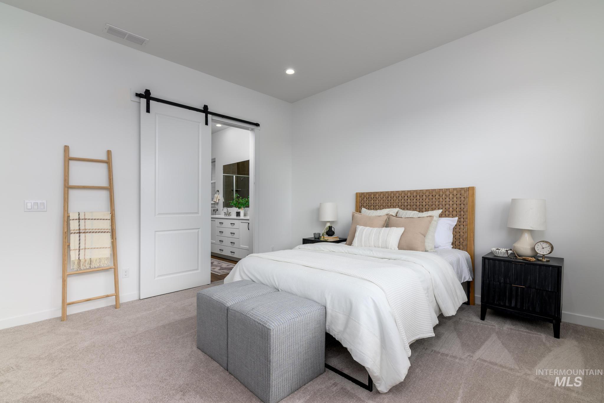Carpeted bedroom featuring a barn door, ensuite bathroom, and recessed lighting