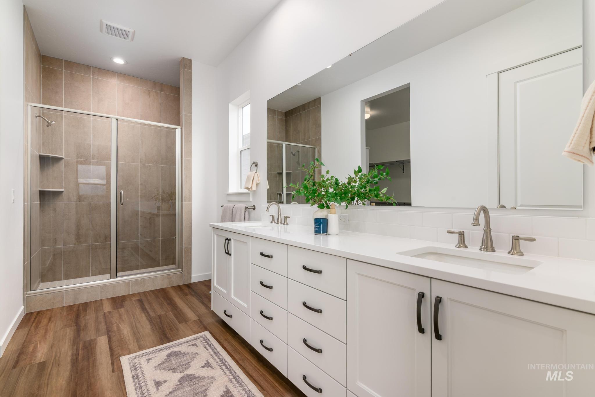 Bathroom with a shower stall, double vanity, dark wood-style floors, a closet, and backsplash