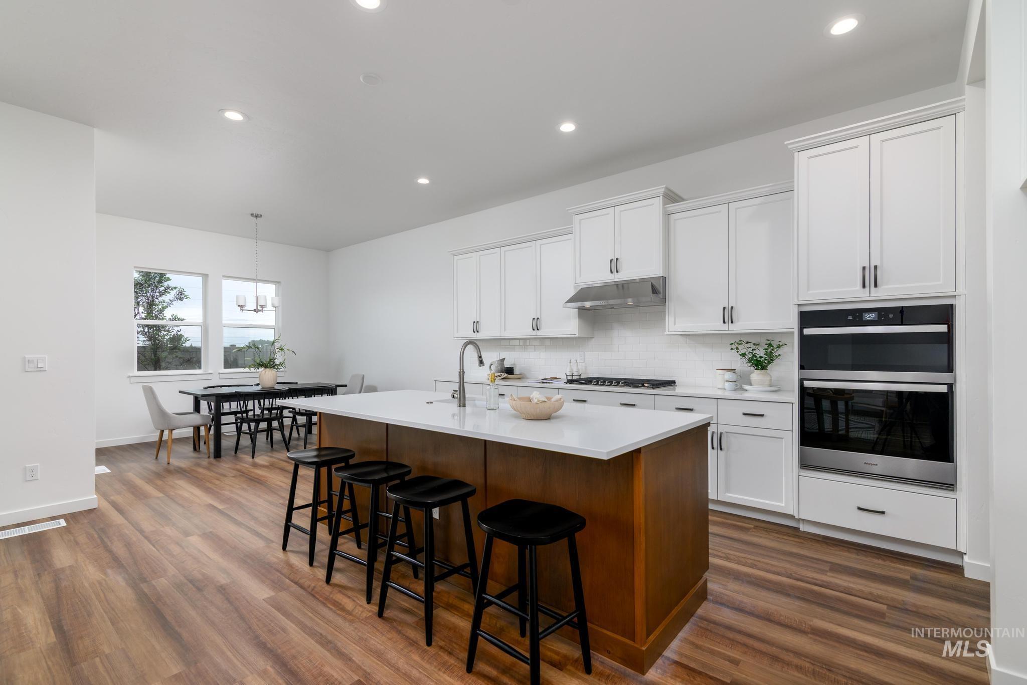 Kitchen with decorative light fixtures, decorative backsplash, white cabinets, a center island with sink, and recessed lighting