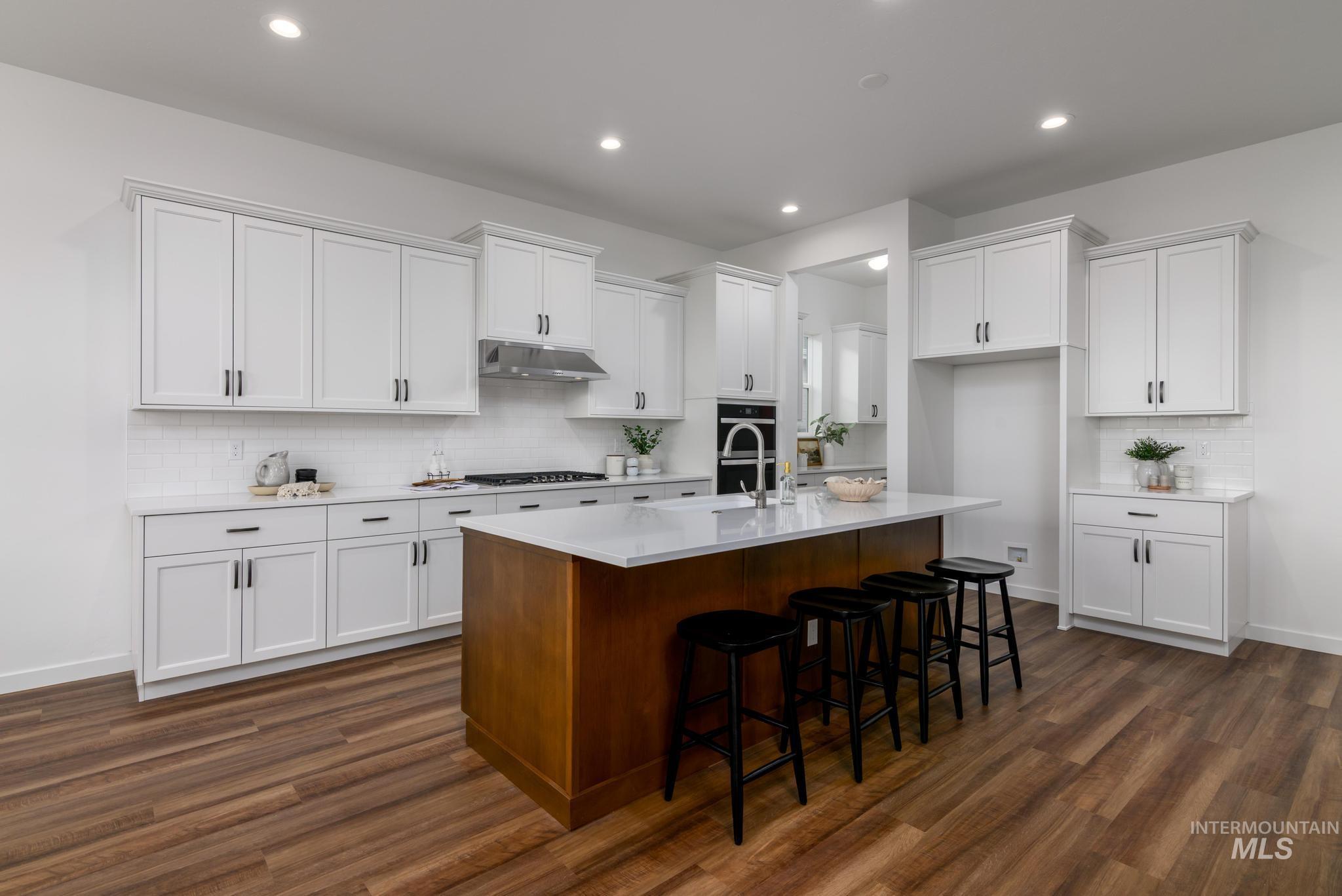 Kitchen featuring tasteful backsplash, white cabinets, a kitchen breakfast bar, an island with sink, and recessed lighting