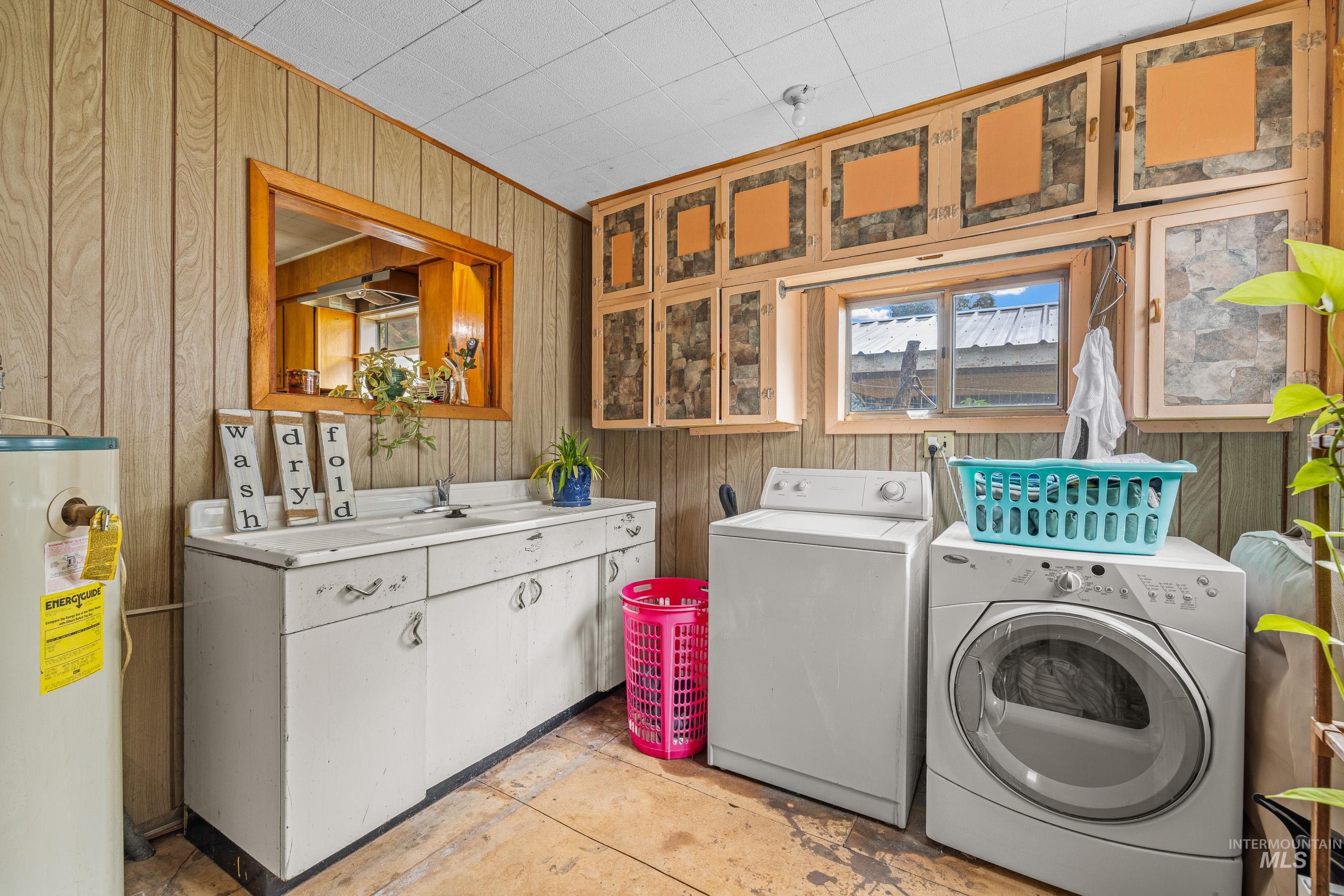 Laundry room featuring wood walls, water heater, and separate washer and dryer