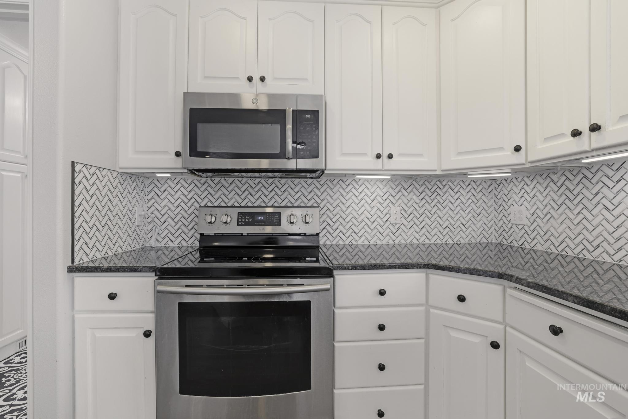 Kitchen featuring appliances with stainless steel finishes, white cabinets, dark stone counters, and tasteful backsplash