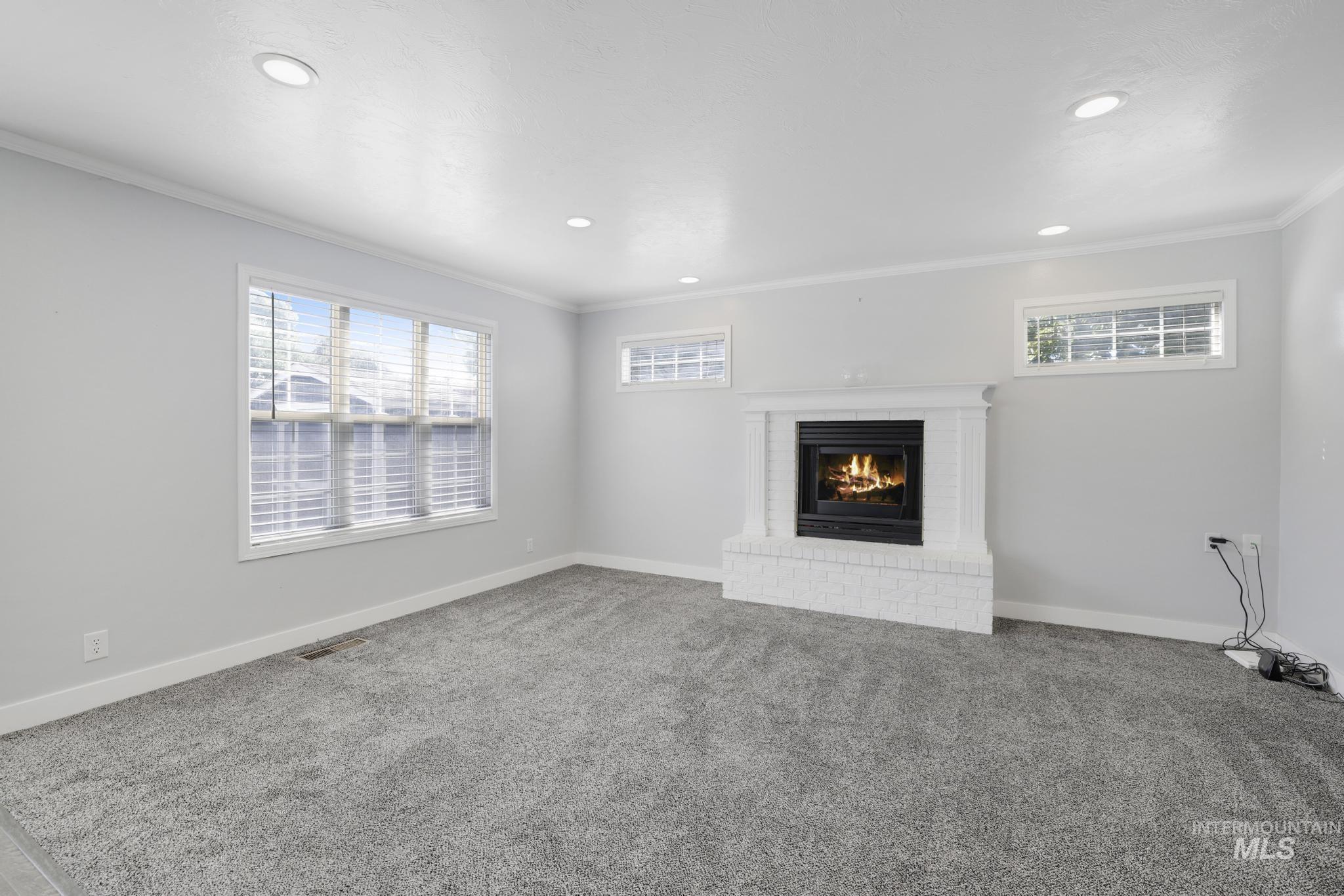 Unfurnished living room featuring ornamental molding, carpet flooring, a brick fireplace, and recessed lighting