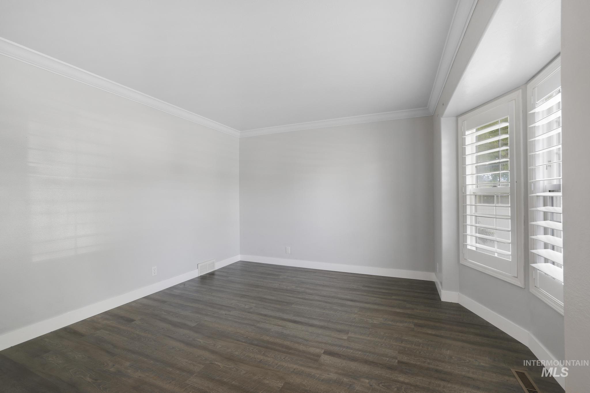 Empty room featuring ornamental molding and dark wood-style floors
