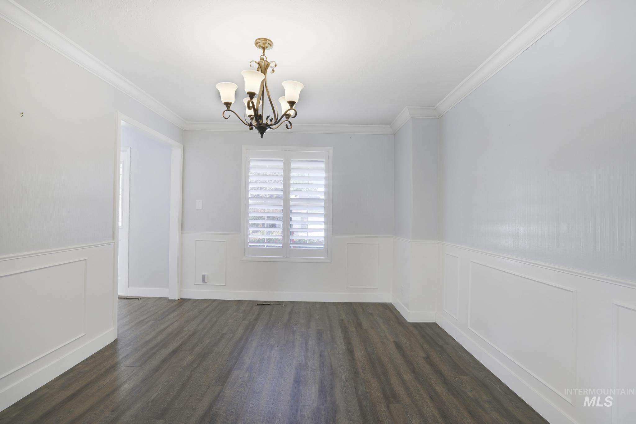 Unfurnished dining area featuring ornamental molding, dark wood-style flooring, a chandelier, wainscoting, and a decorative wall