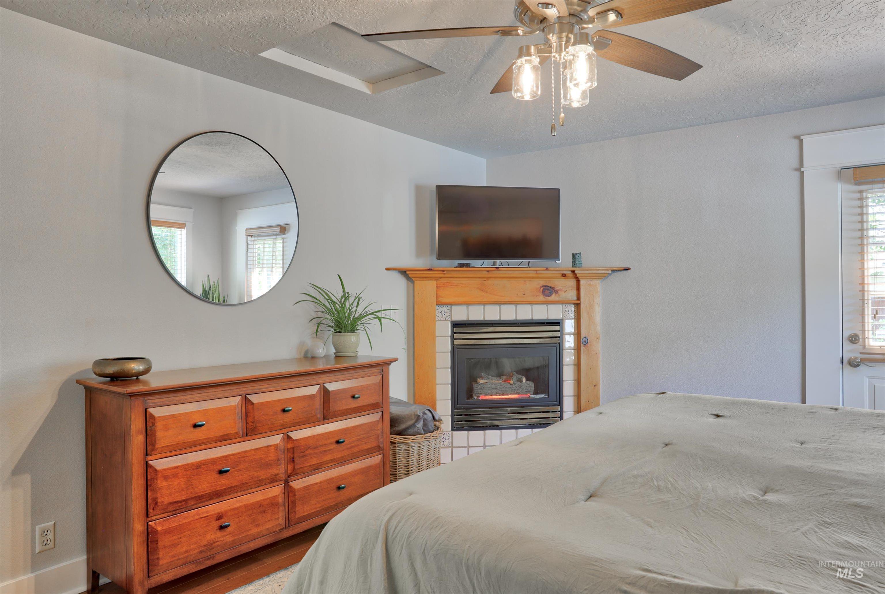 Bedroom with a textured ceiling, a ceiling fan, wood finished floors, and a tiled fireplace