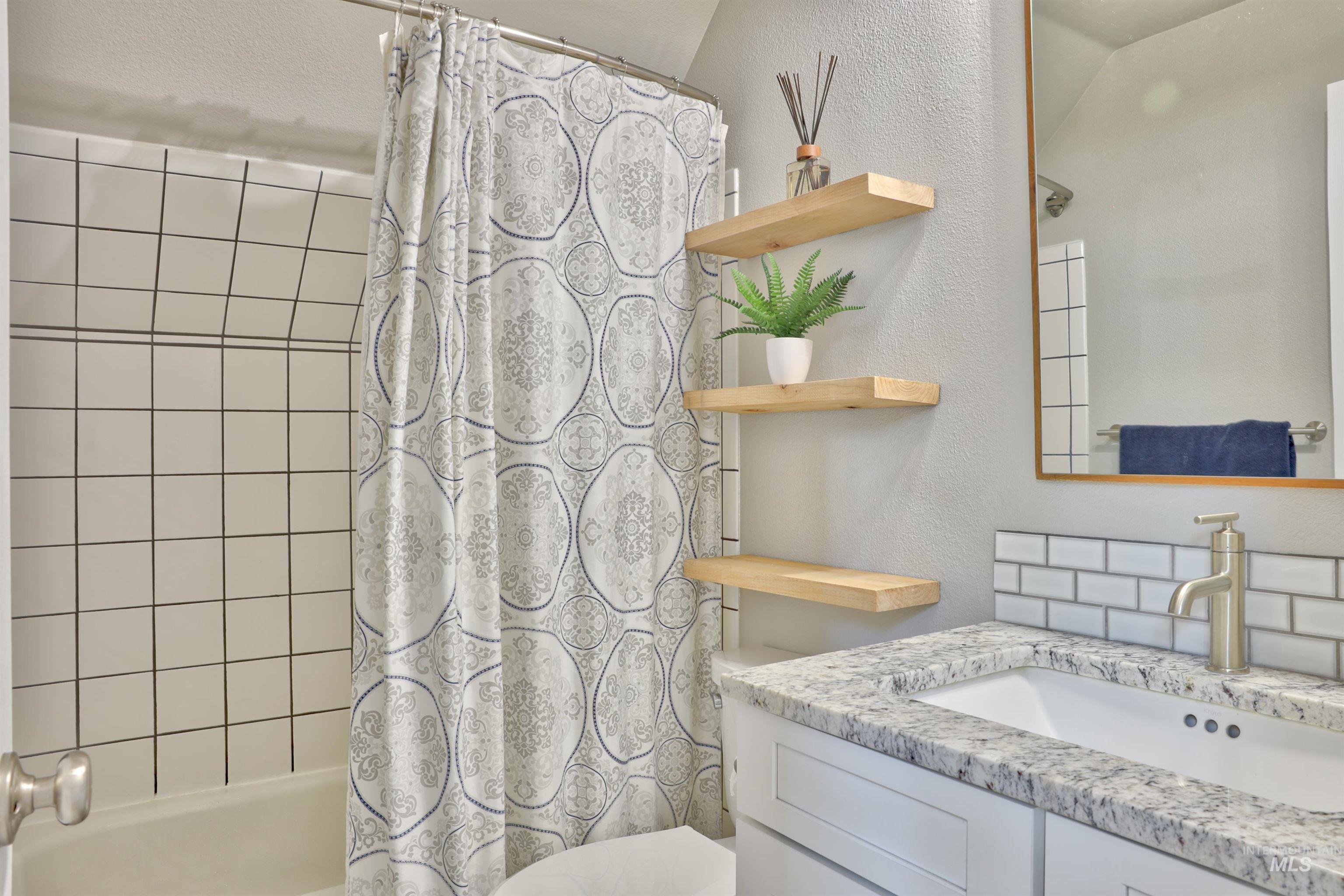 Full bath featuring shower / bath combo with shower curtain, a textured wall, and vanity