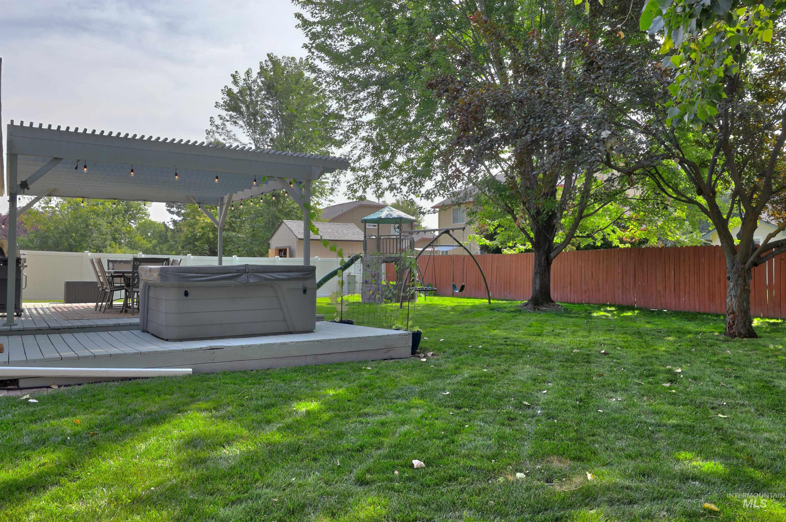 Fenced backyard with a playground, a hot tub, and a deck