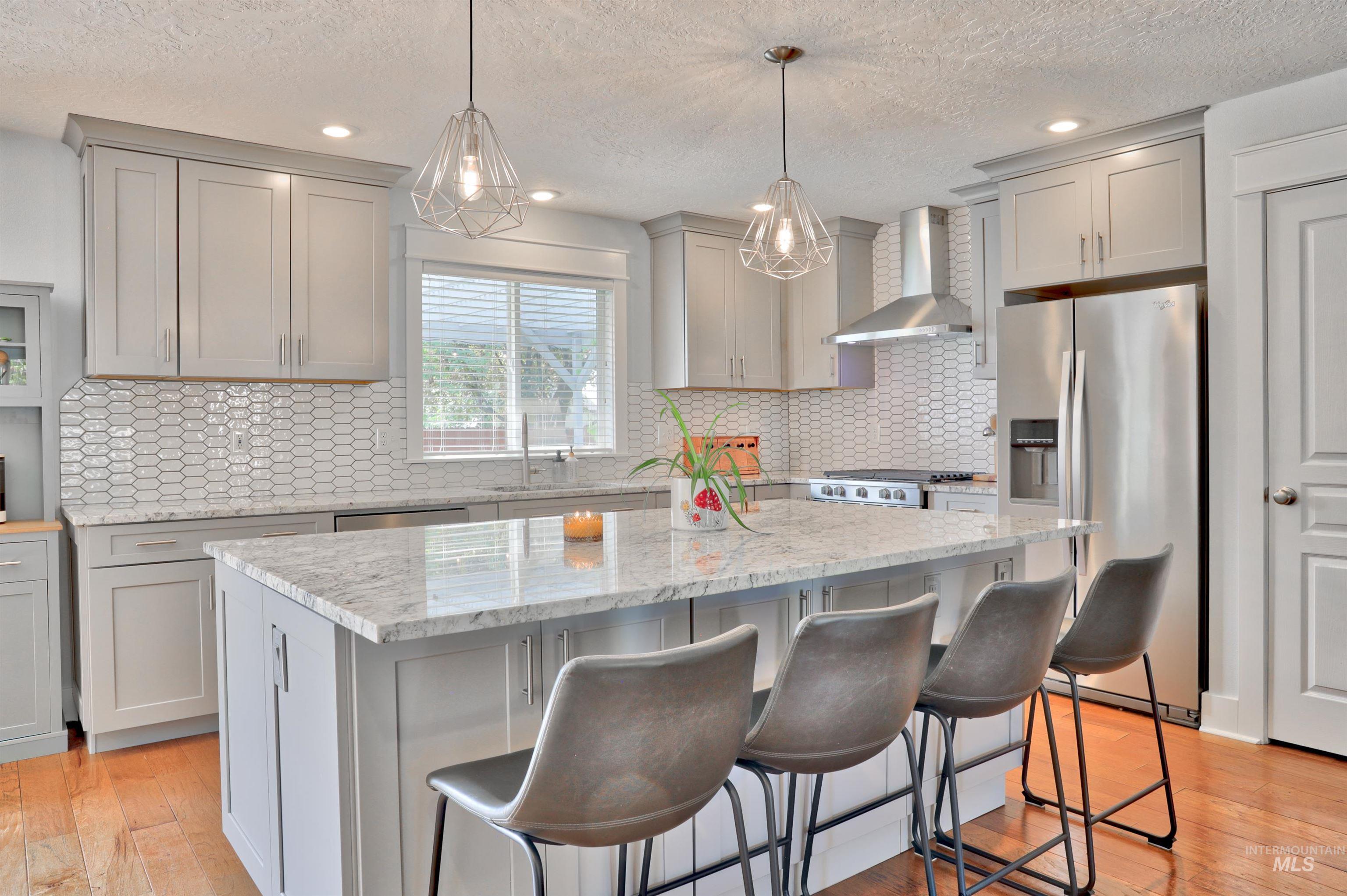 Kitchen featuring gray cabinetry, stainless steel appliances, light stone countertops, light wood finished floors, and a textured ceiling