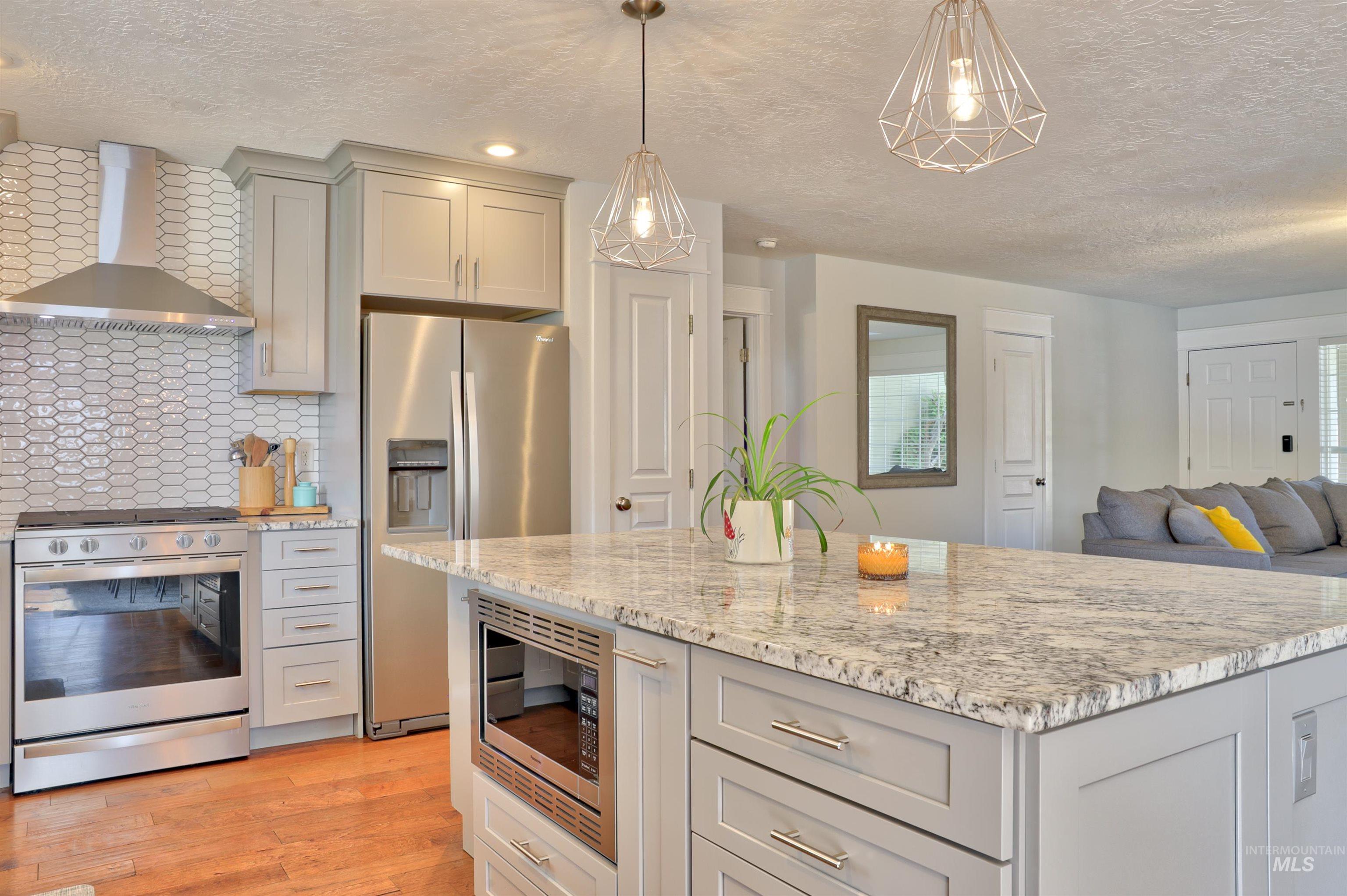 Kitchen with appliances with stainless steel finishes, gray cabinetry, wall chimney exhaust hood, a textured ceiling, and backsplash