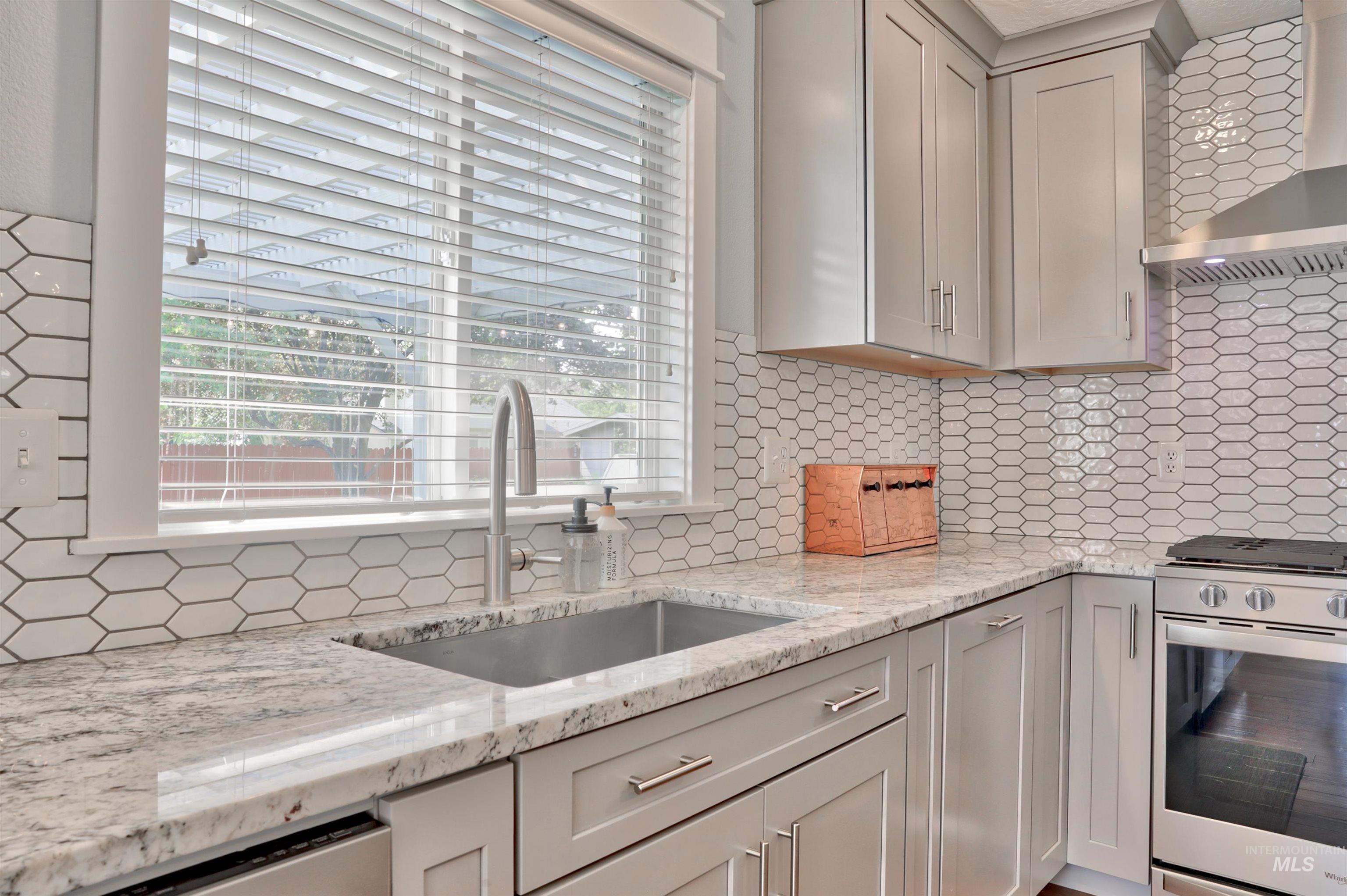 Kitchen featuring tasteful backsplash, stainless steel gas stove, wall chimney range hood, and light stone counters
