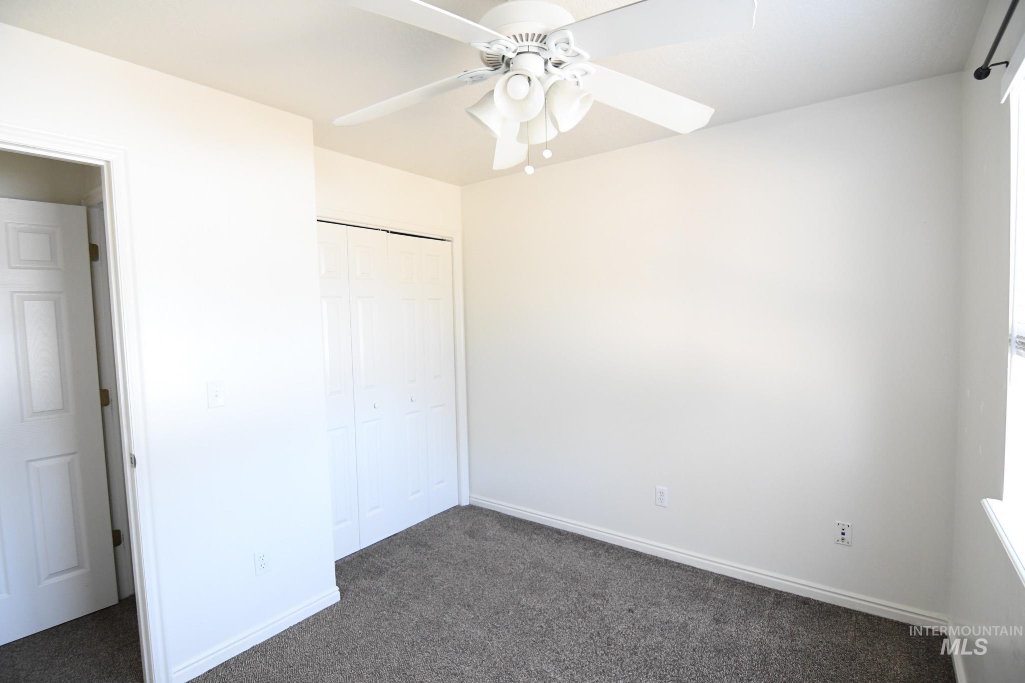 Unfurnished bedroom featuring dark carpet, a closet, and ceiling fan