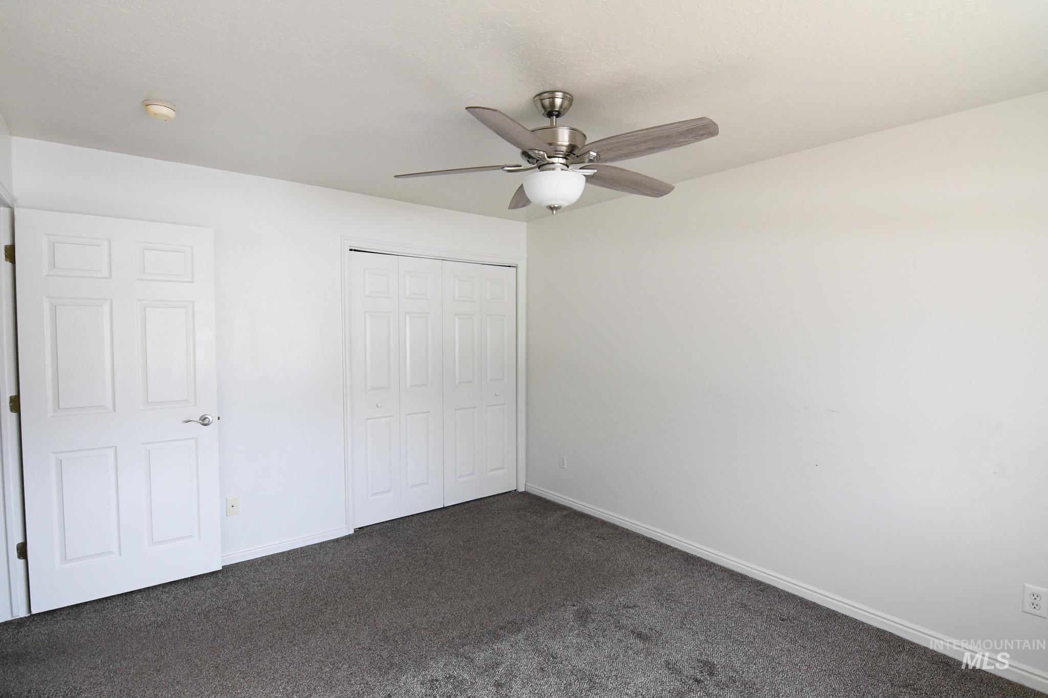 Unfurnished bedroom featuring dark carpet, a closet, and a ceiling fan