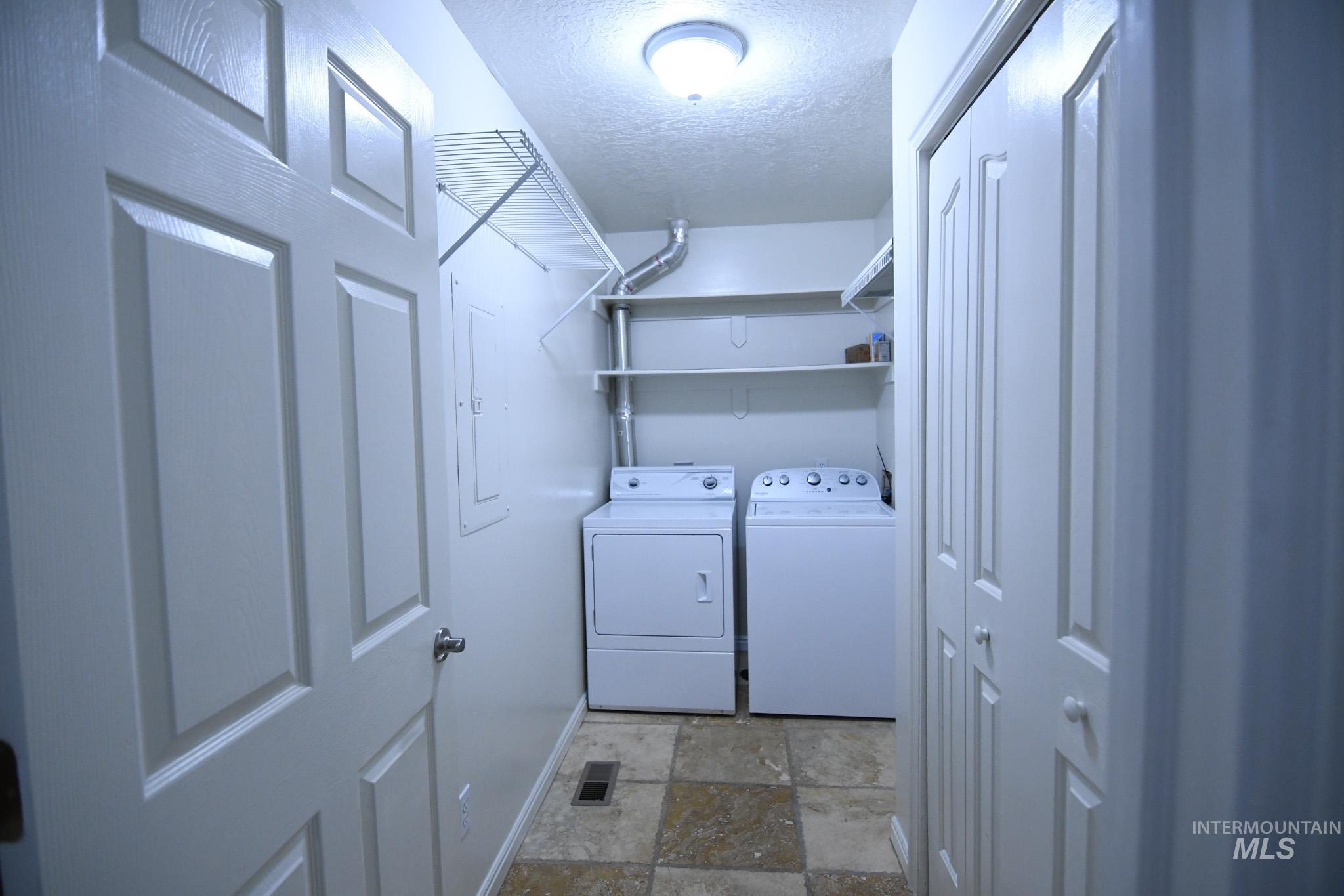 Laundry room featuring a textured ceiling, separate washer and dryer, dark stone finish floors, and electric panel