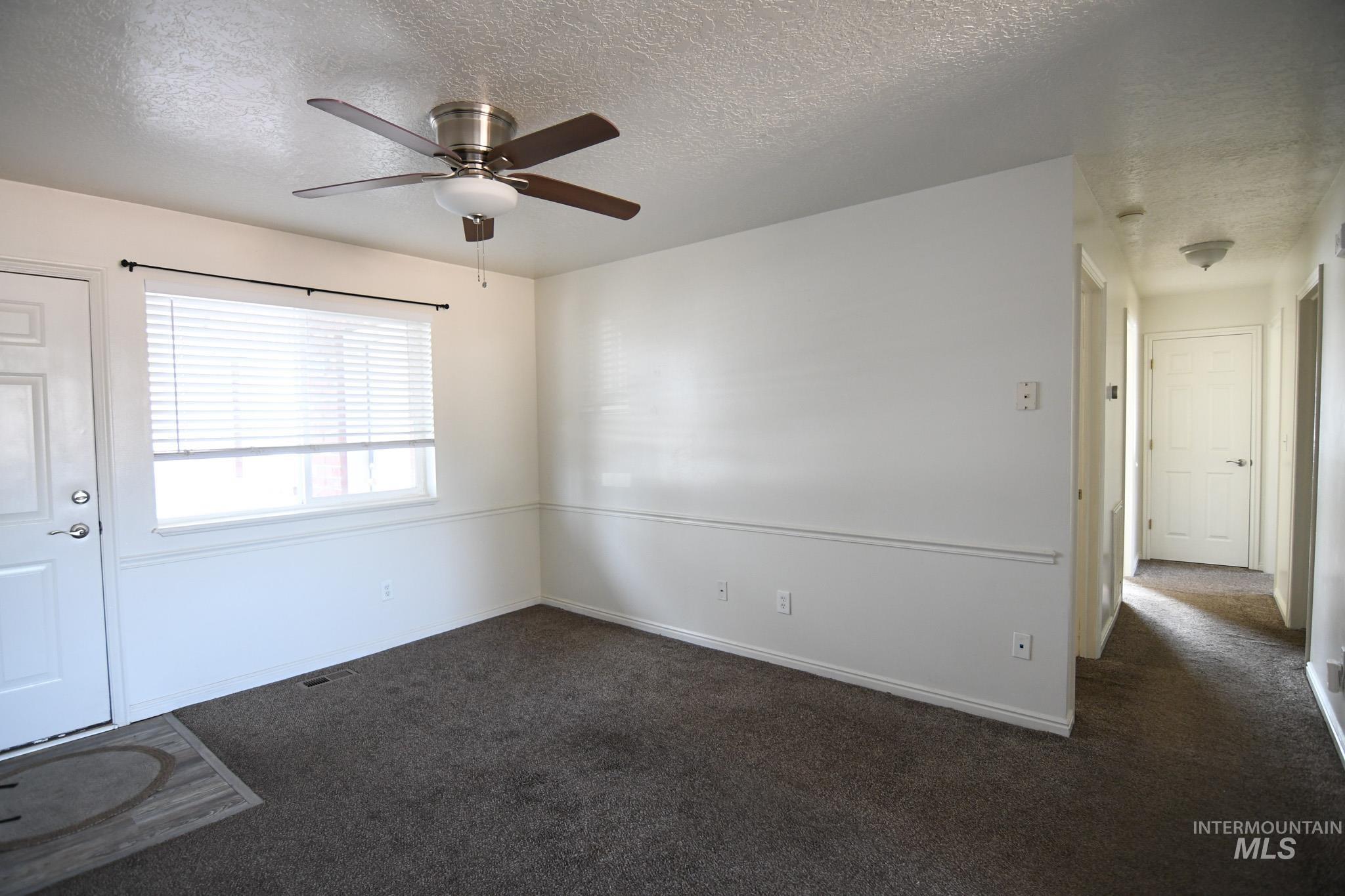 Spare room featuring dark colored carpet, a textured ceiling, and ceiling fan