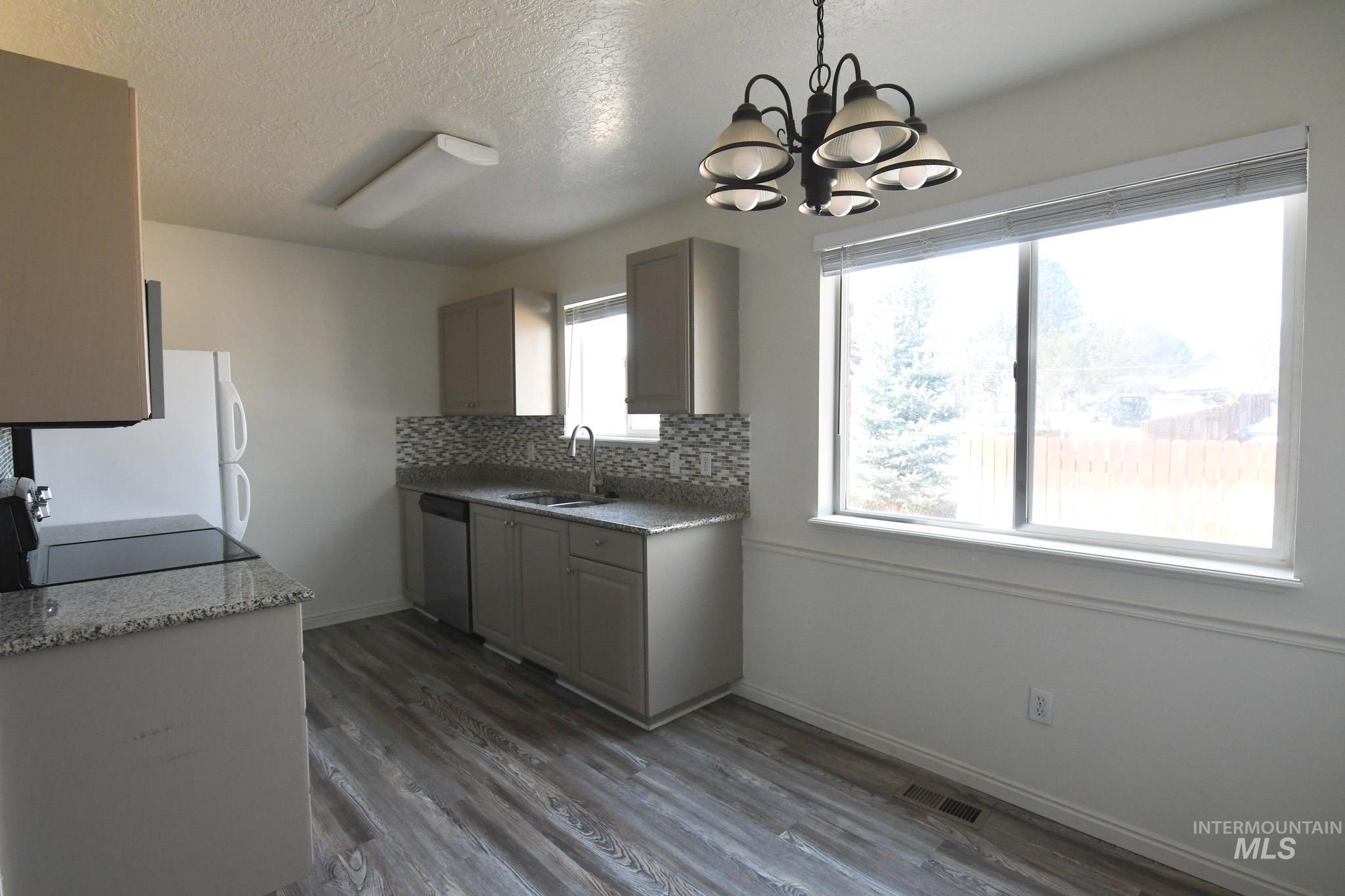 Kitchen featuring dark wood finished floors, a chandelier, tasteful backsplash, a textured ceiling, and white appliances