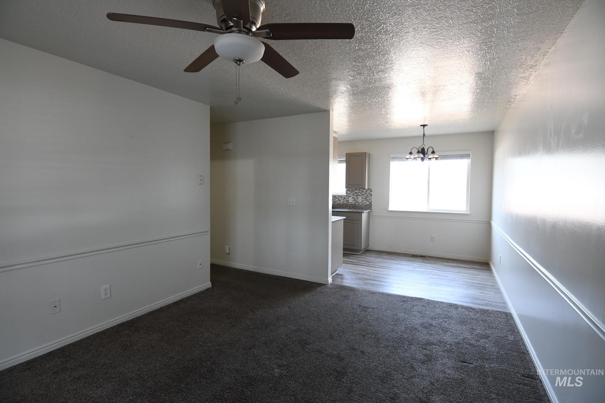 Unfurnished living room with a chandelier, dark carpet, a textured ceiling, and ceiling fan