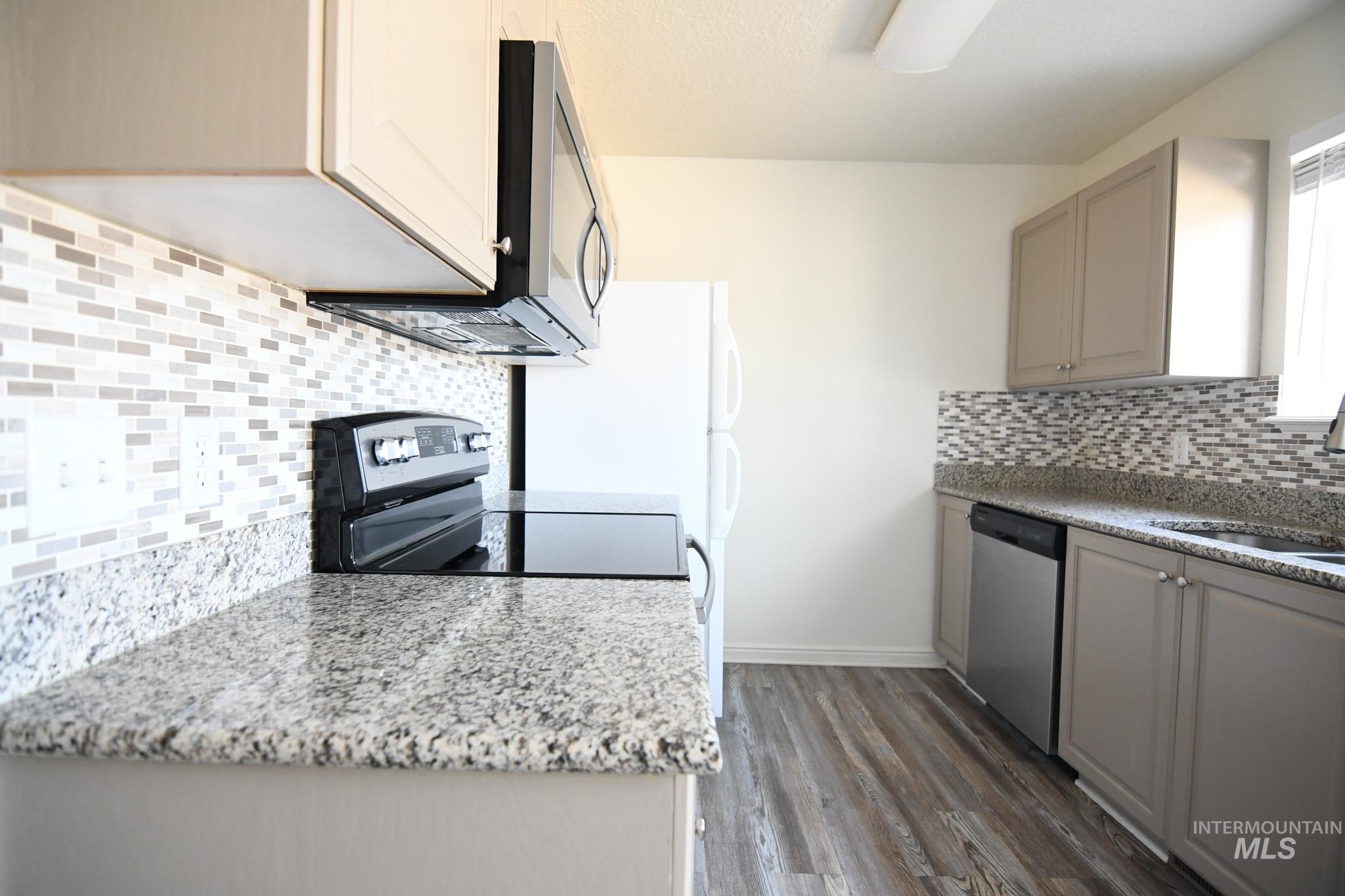 Kitchen featuring tasteful backsplash, light stone counters, appliances with stainless steel finishes, light wood-style floors, and gray cabinets