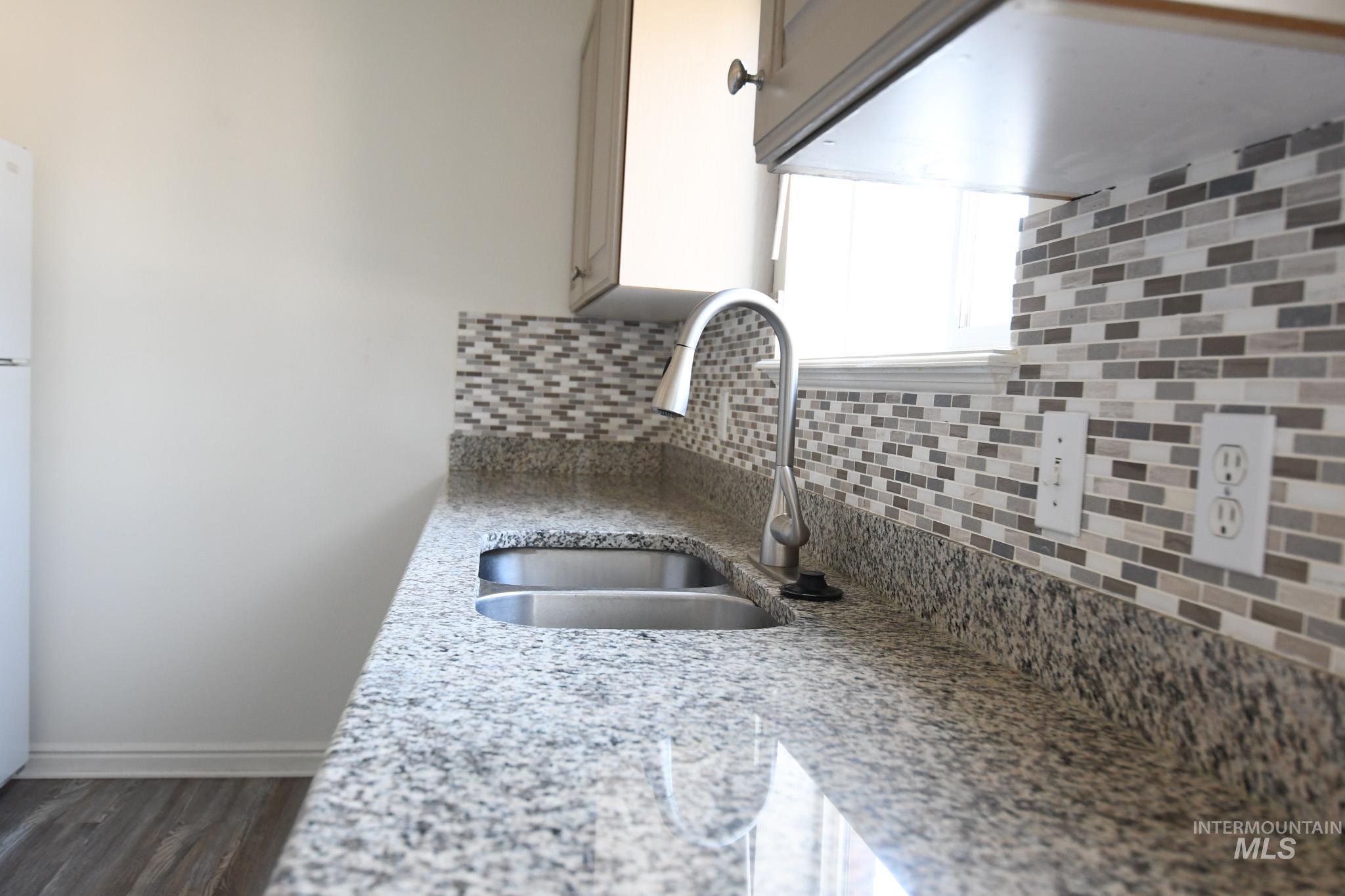 Kitchen with light stone counters, backsplash, dark wood-type flooring, and freestanding refrigerator