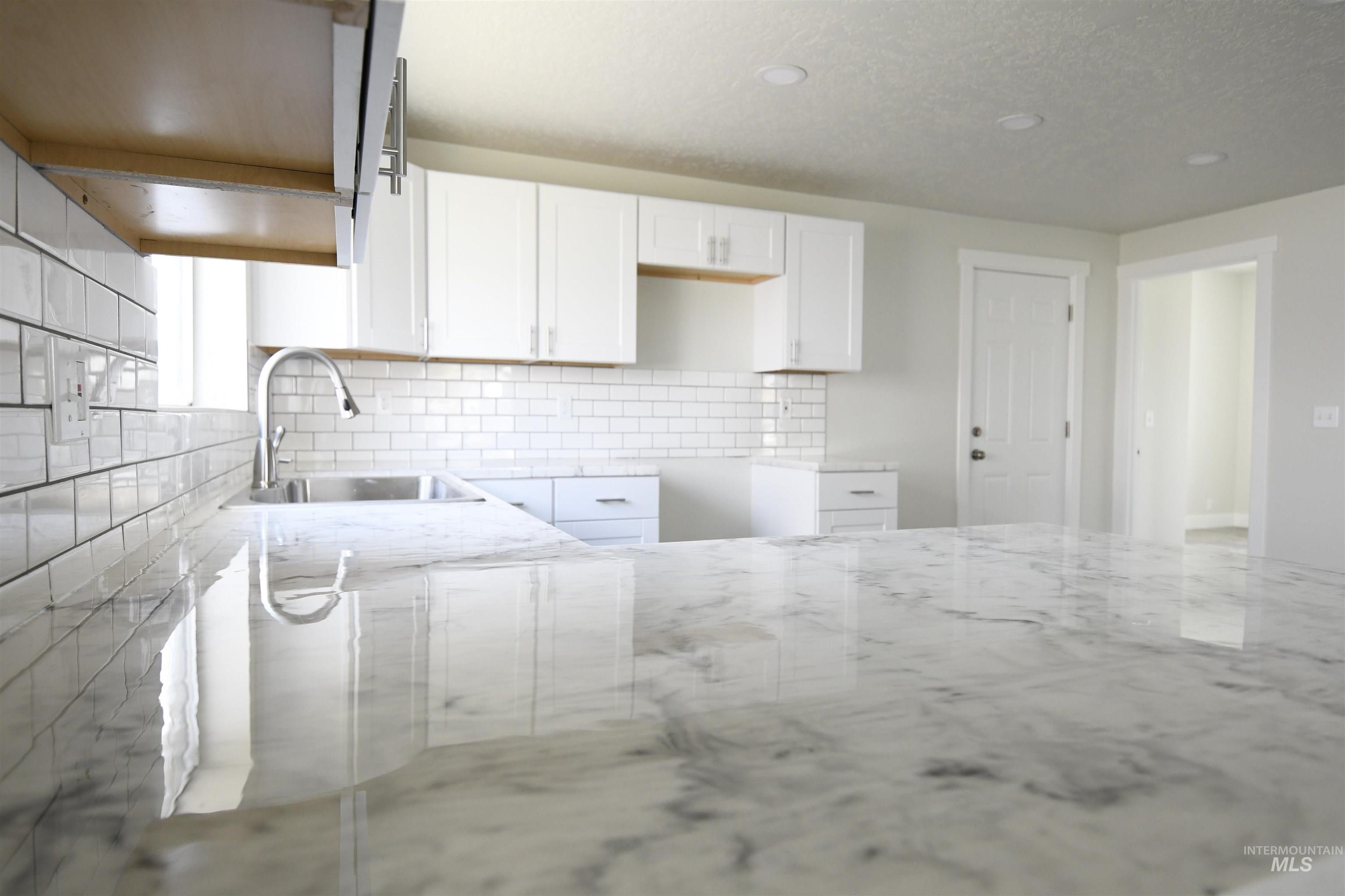 Kitchen featuring light stone counters, decorative backsplash, white cabinets, a textured ceiling, and recessed lighting