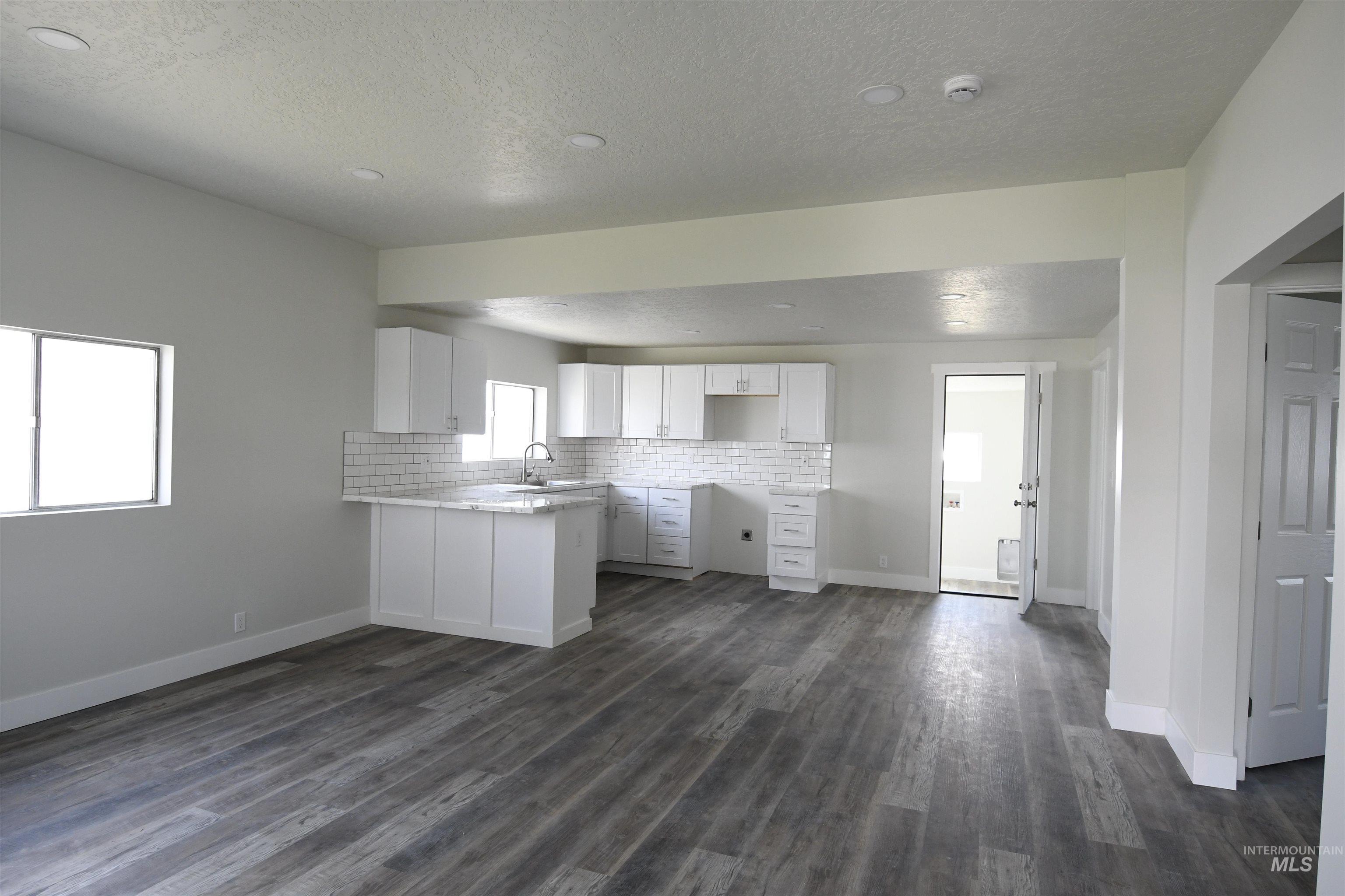 Kitchen featuring a peninsula, a textured ceiling, tasteful backsplash, white cabinets, and dark wood-type flooring
