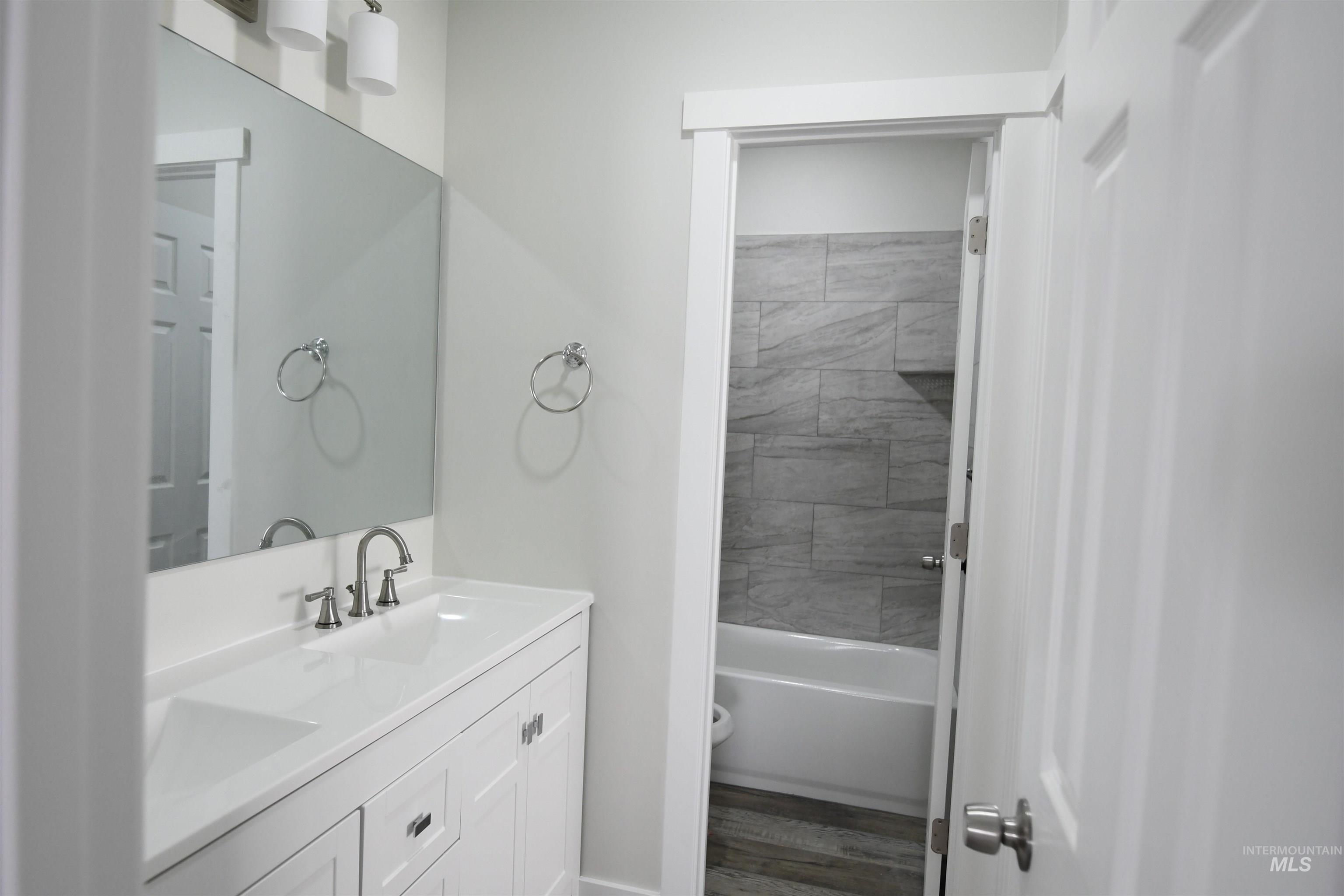 Bathroom featuring double vanity, dark wood-style flooring, and bathing tub / shower combination