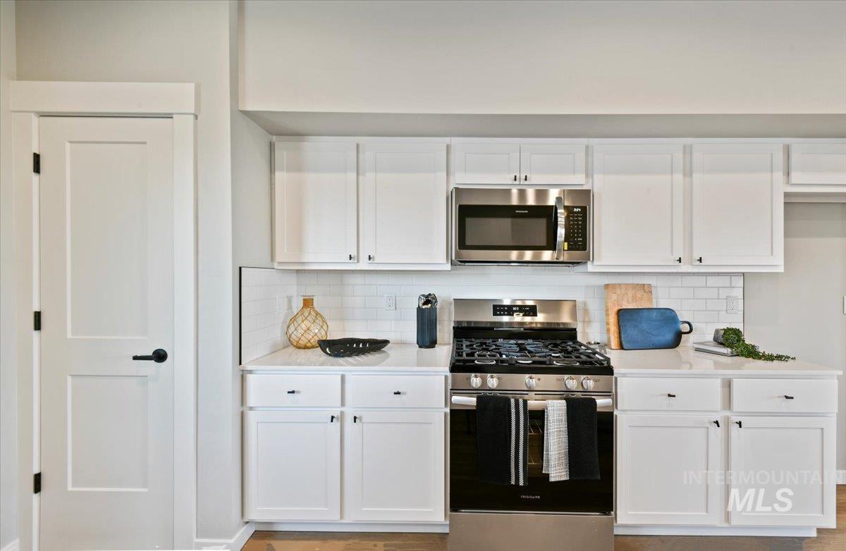 Kitchen with stainless steel appliances, white cabinetry, decorative backsplash, and light stone counters
