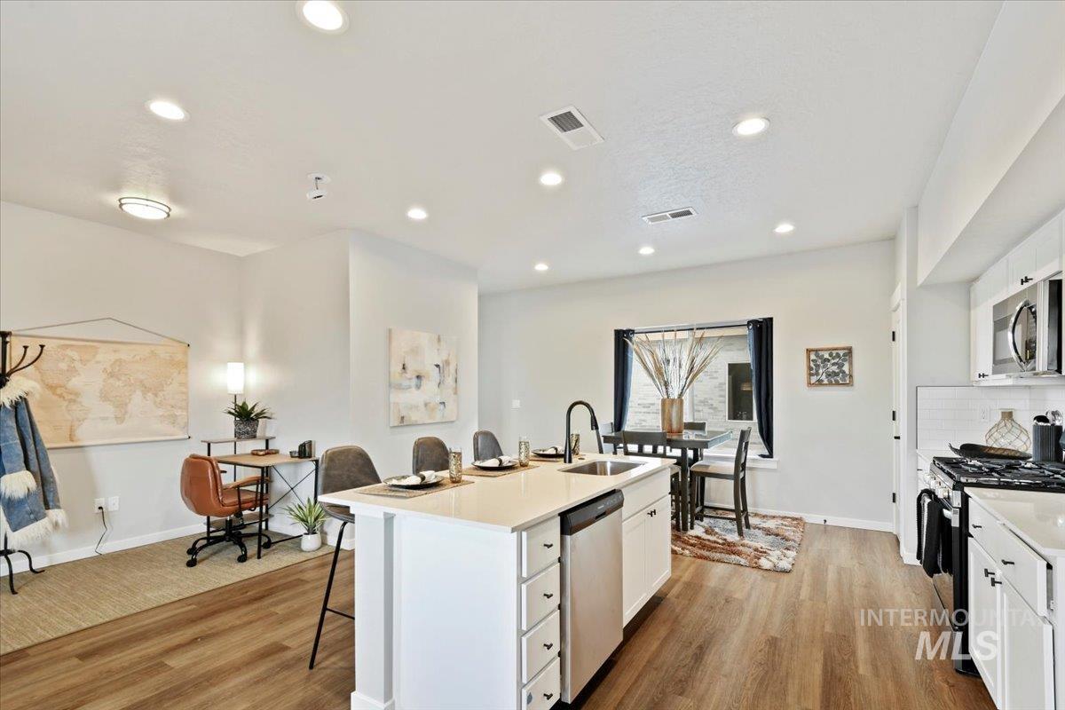Kitchen featuring white cabinetry, stainless steel appliances, a kitchen island with sink, light wood-style floors, and a kitchen bar