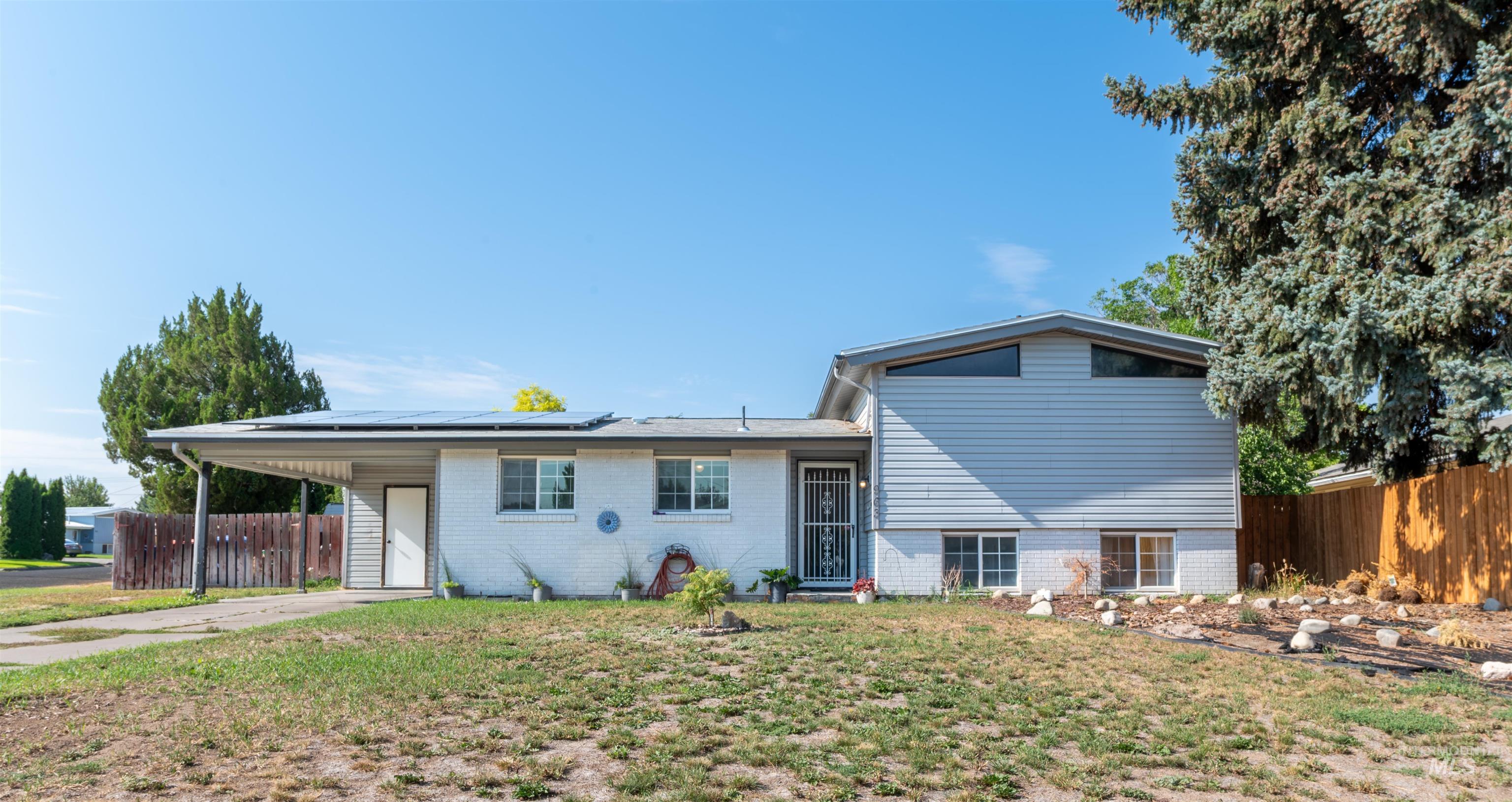Rear view of house with an attached carport, roof mounted solar panels, concrete driveway, and brick siding