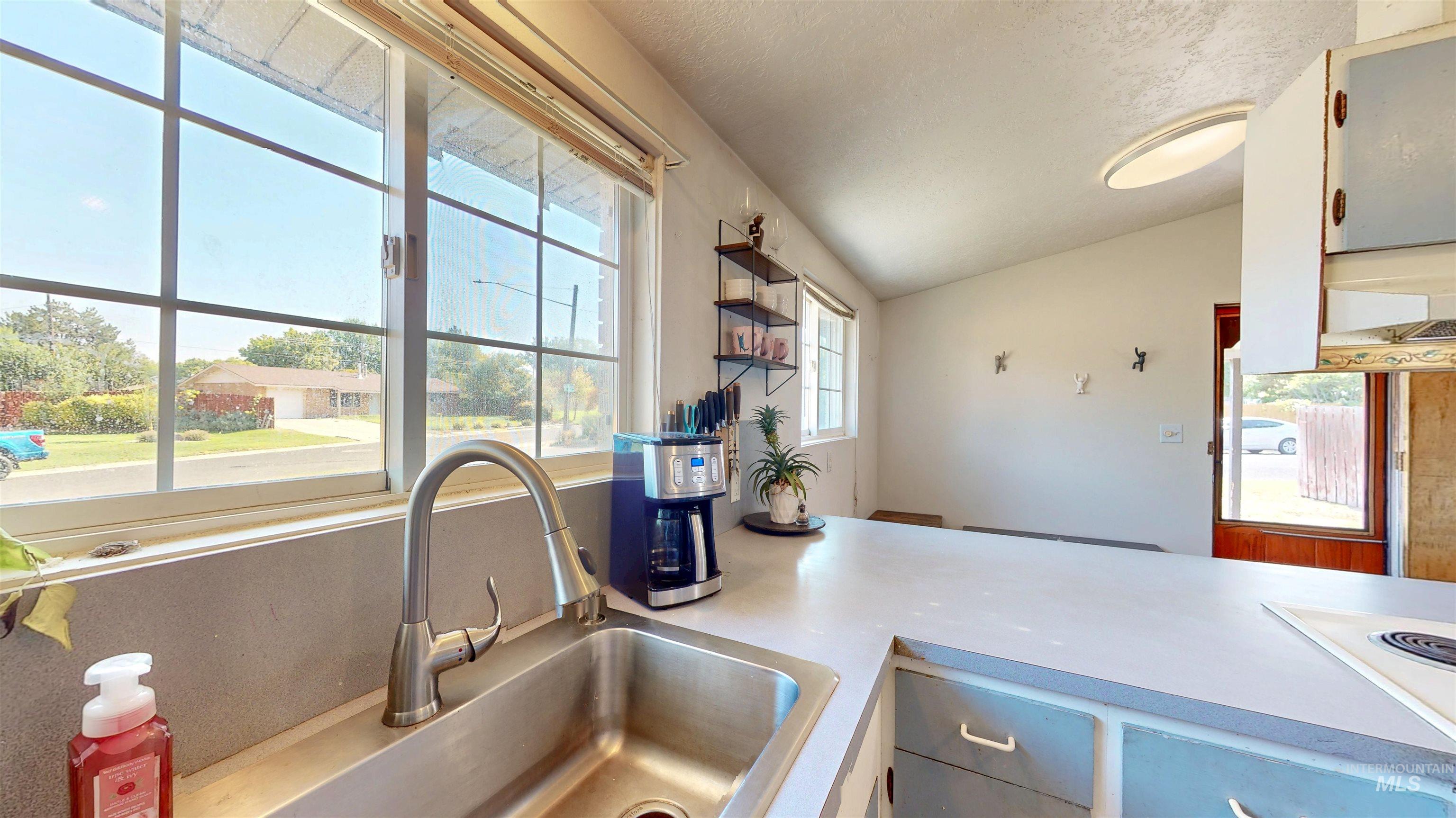 Kitchen featuring healthy amount of natural light, lofted ceiling, light countertops, range hood, and open shelves