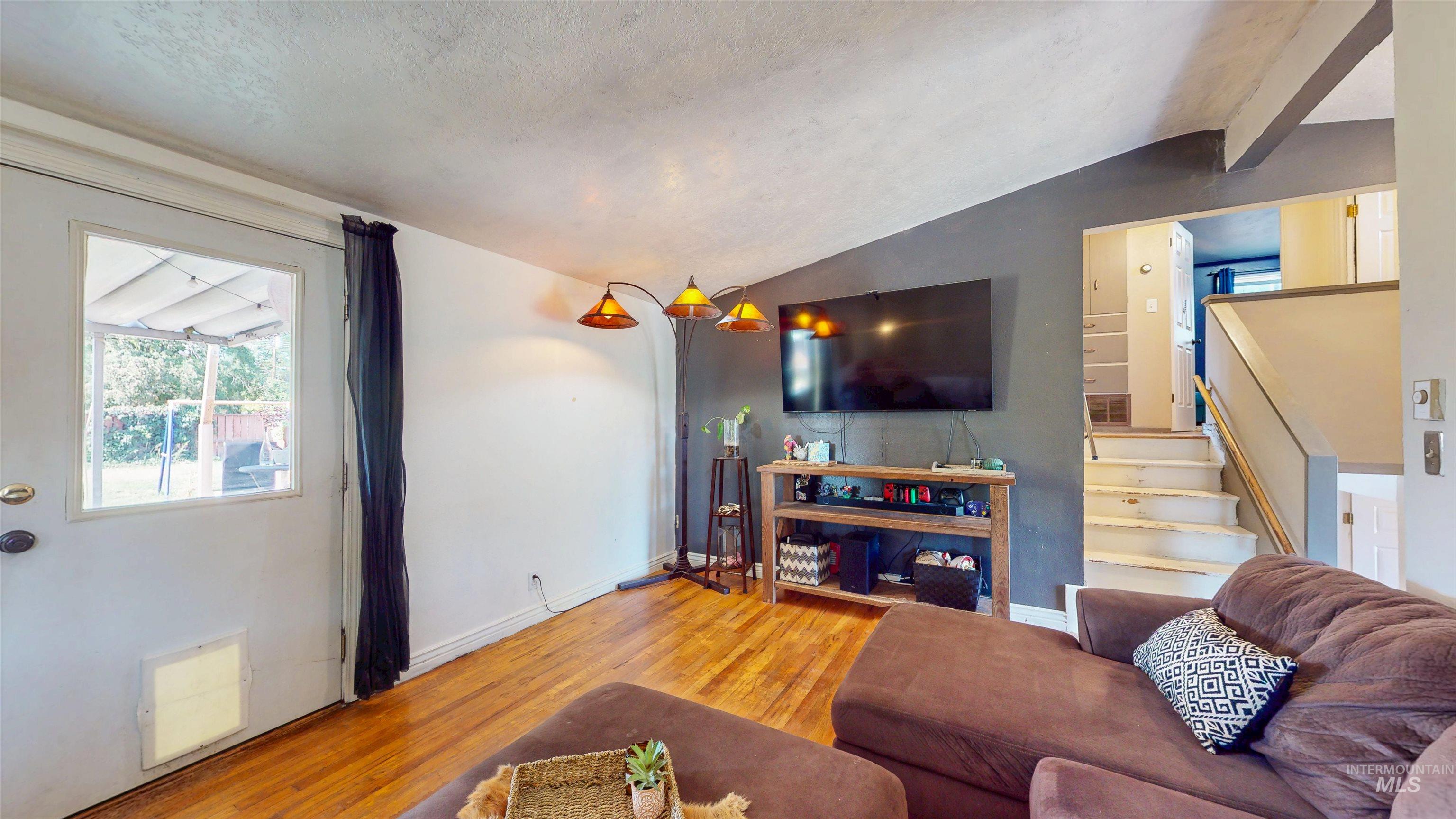 Living area featuring lofted ceiling, wood finished floors, and stairs
