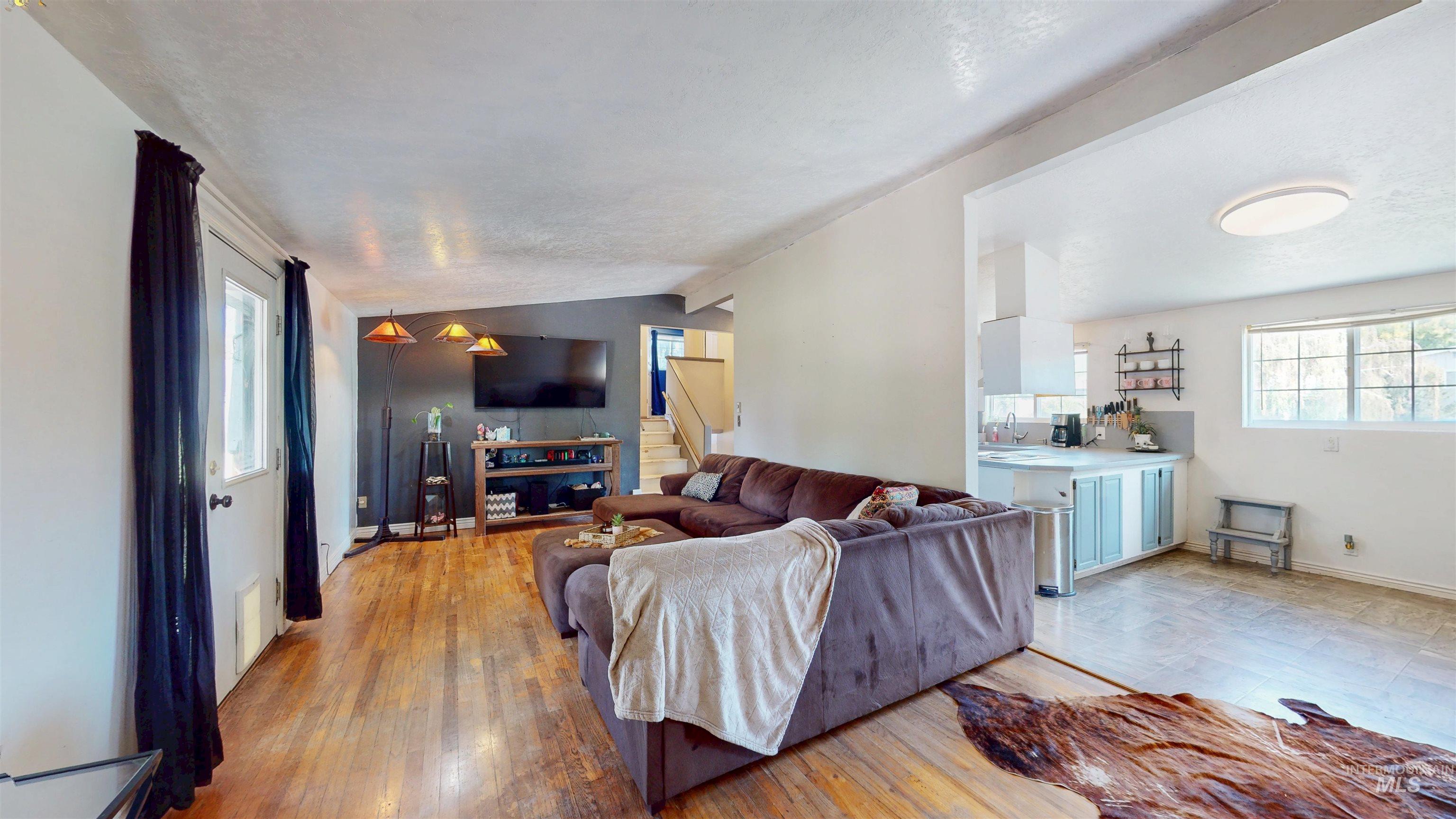 Living room with light wood-style floors, vaulted ceiling, and stairs