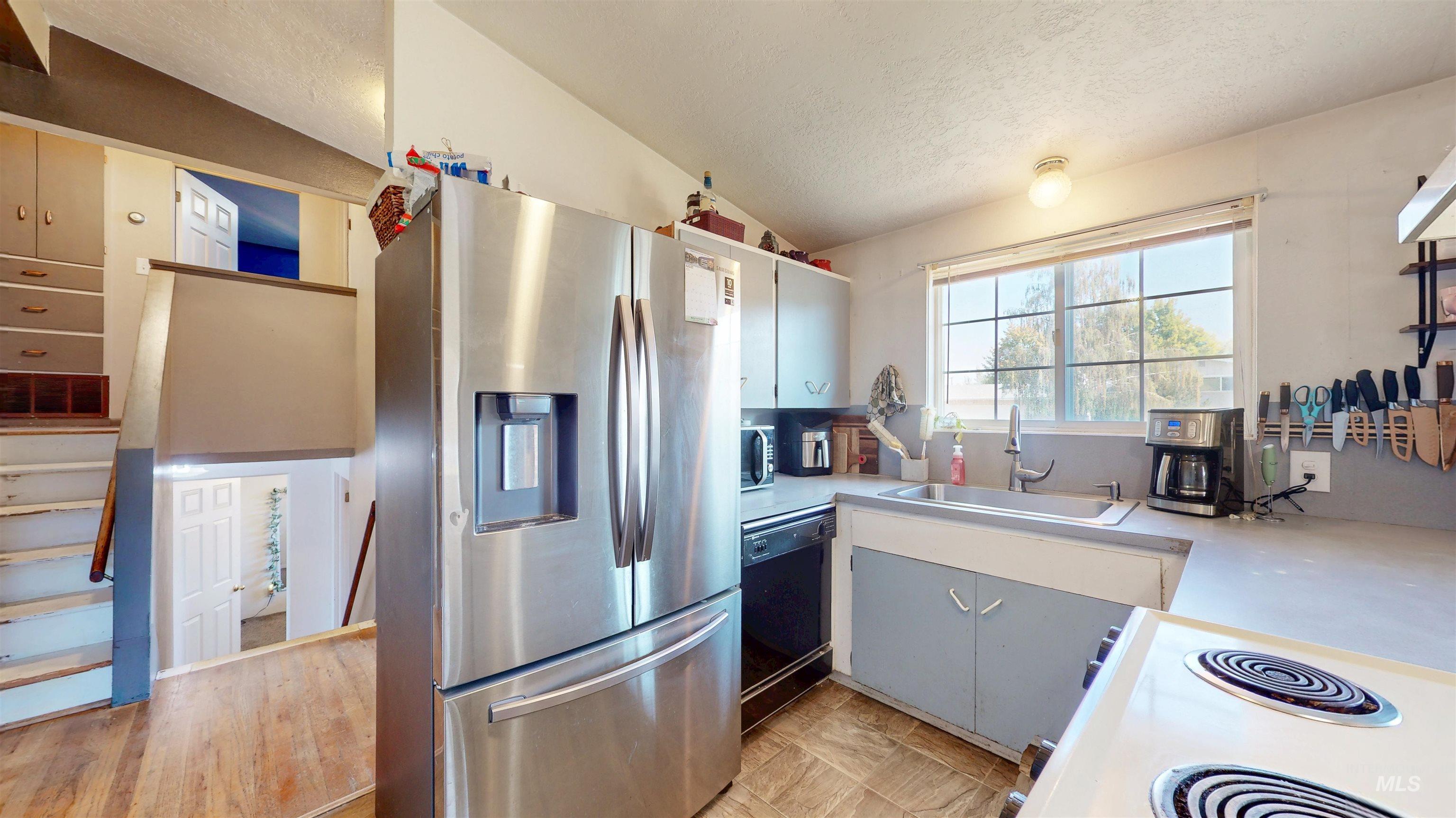 Kitchen with white appliances, light countertops, a textured ceiling, vaulted ceiling, and white cabinets