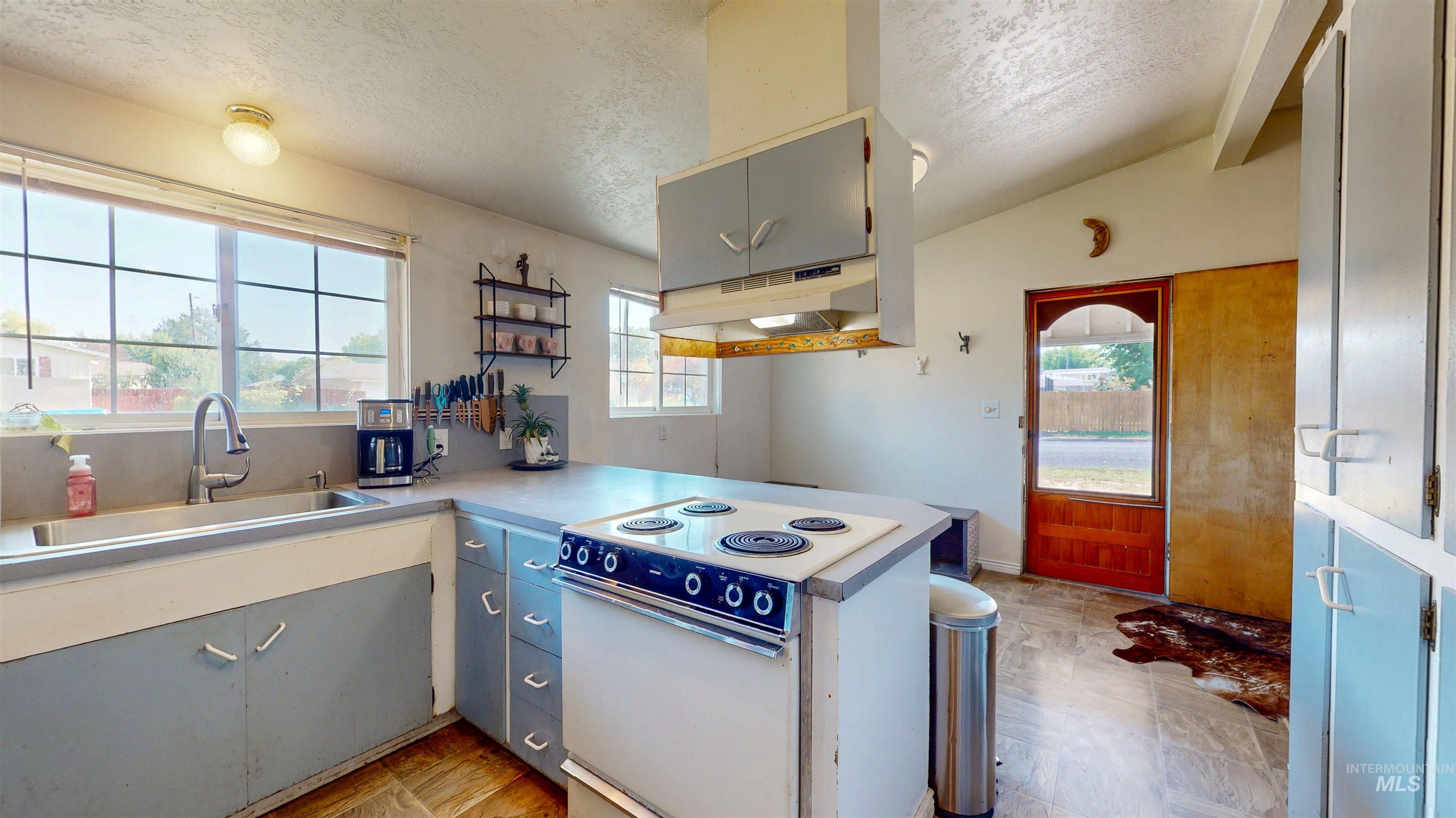 Kitchen featuring white range with electric cooktop, a textured ceiling, under cabinet range hood, light countertops, and a peninsula