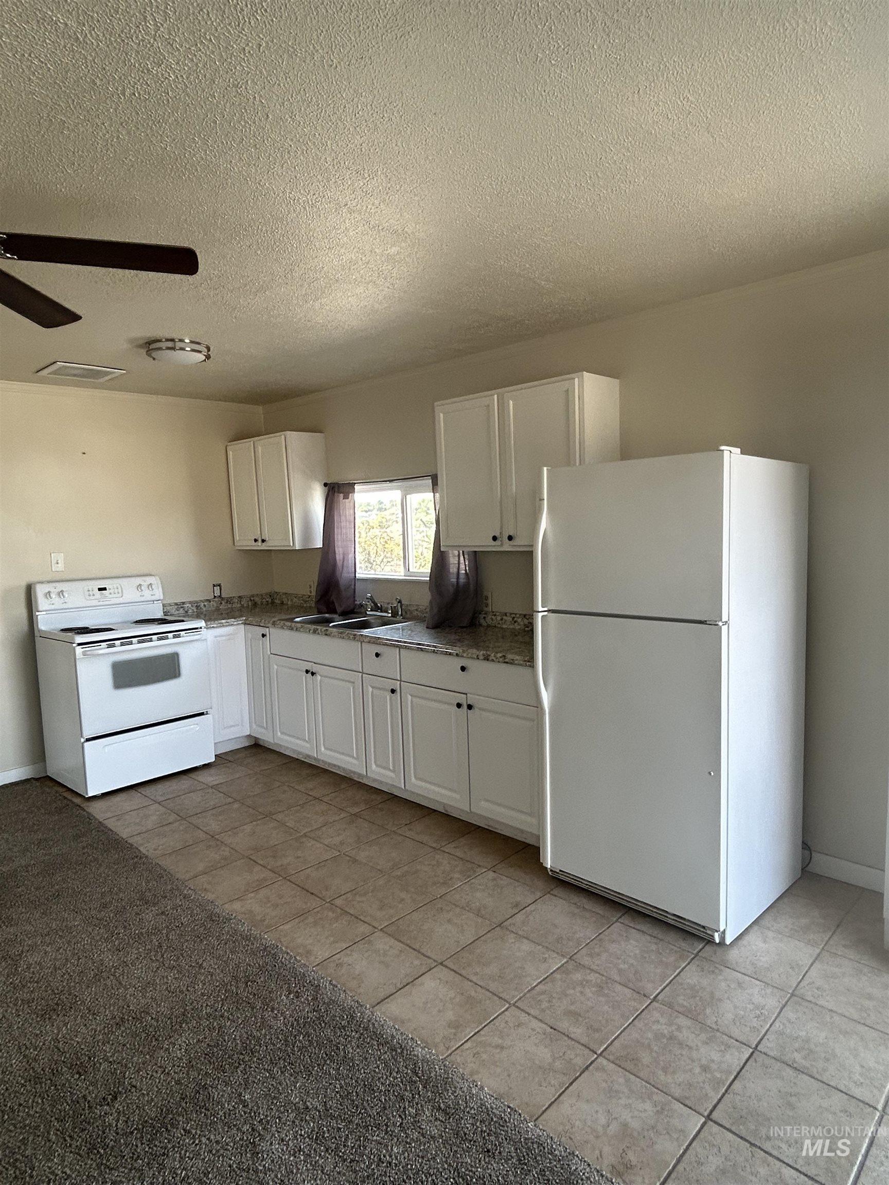 Kitchen with white cabinets, white appliances, a textured ceiling, light tile patterned floors, and a ceiling fan