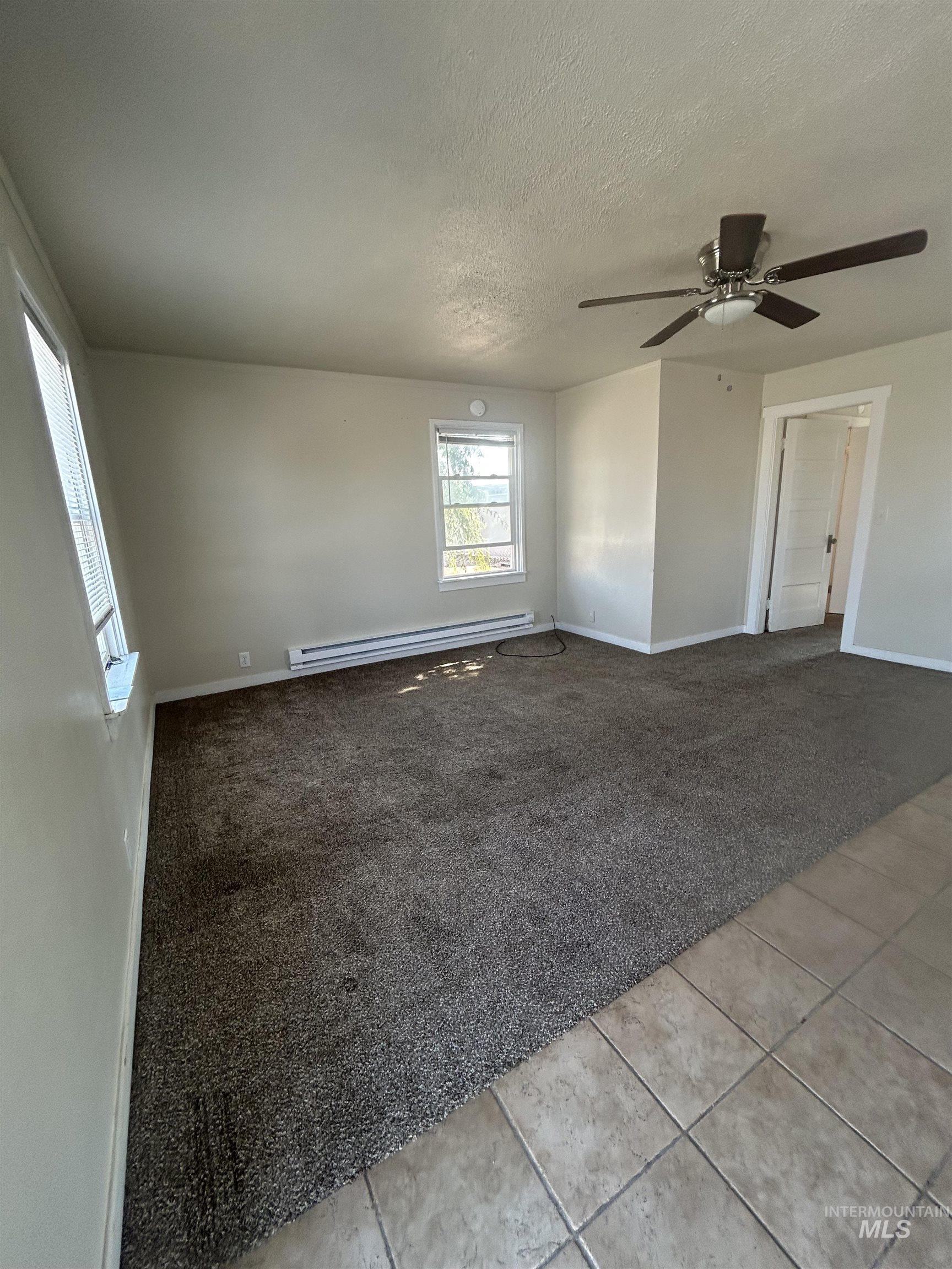 Unfurnished room with light colored carpet, light tile patterned flooring, a textured ceiling, a baseboard radiator, and ceiling fan