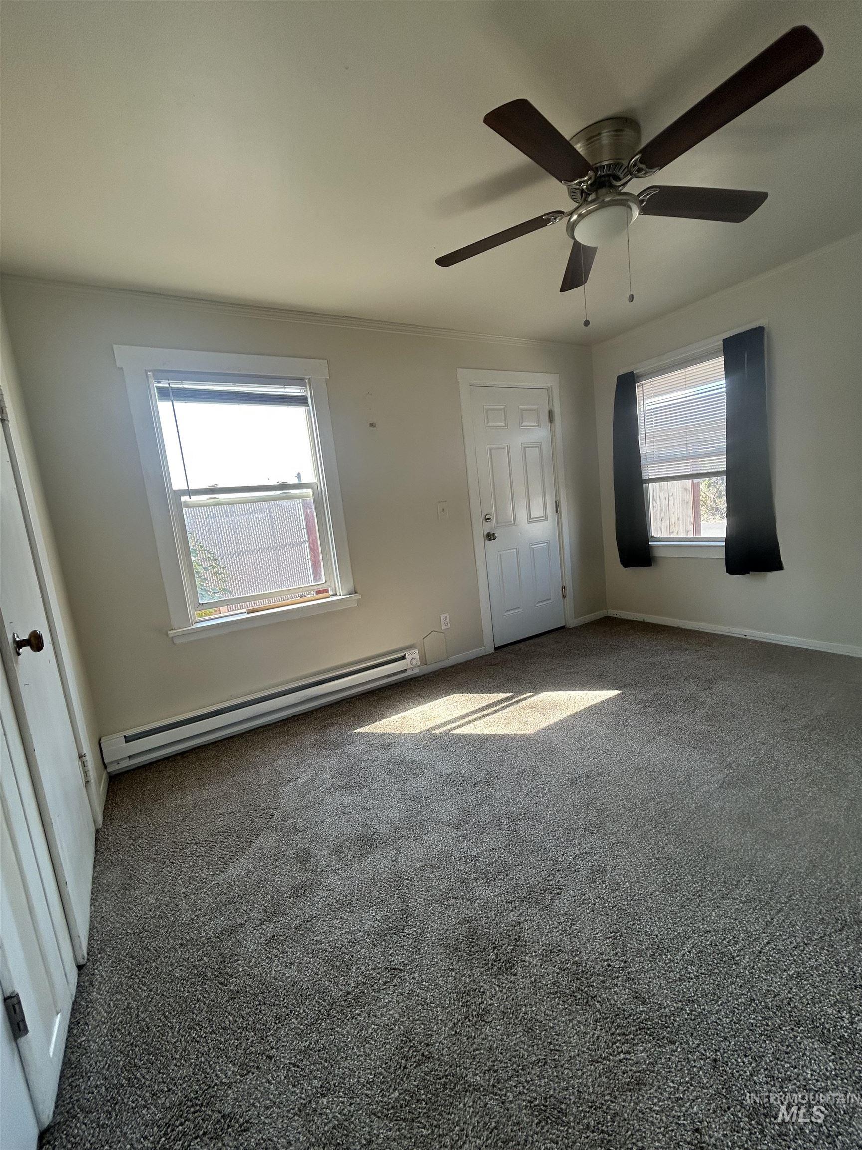 Empty room with a baseboard heating unit, carpet, and a ceiling fan