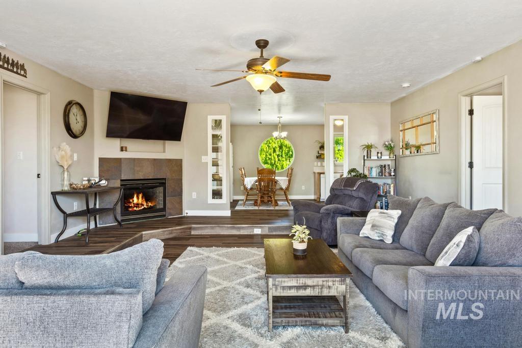 Living room featuring wood finished floors, a tiled fireplace, a ceiling fan, and a textured ceiling