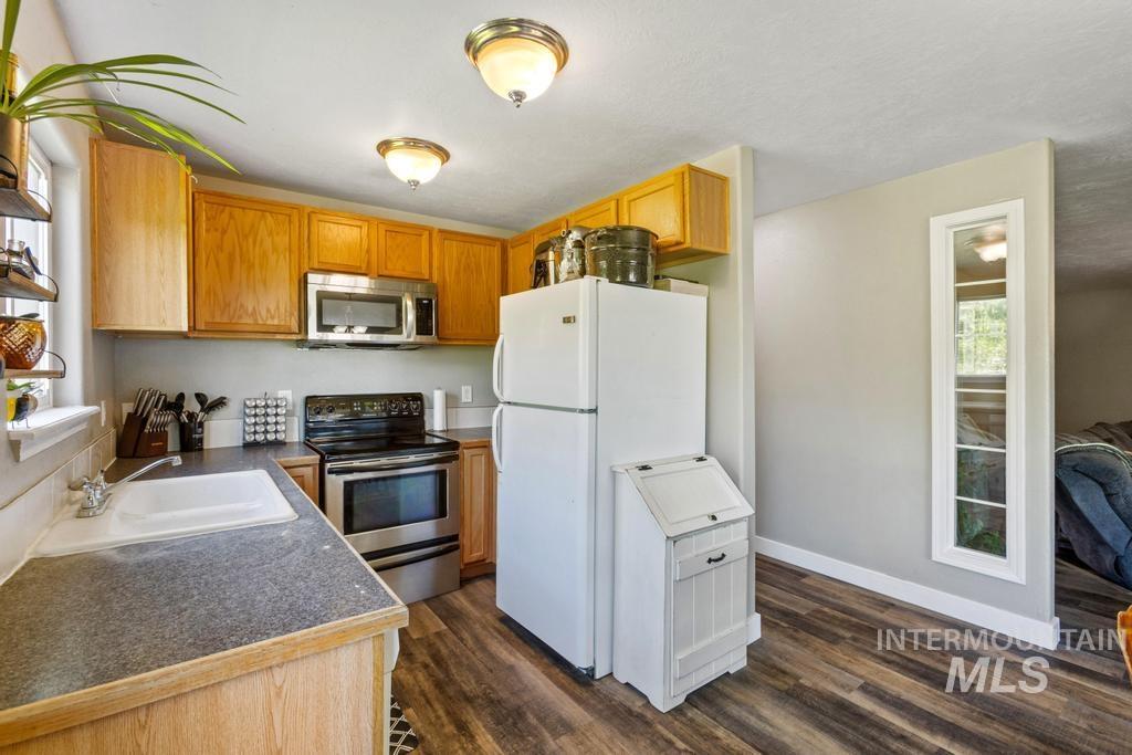 Kitchen with dark countertops, stainless steel appliances, dark wood-type flooring, and brown cabinets