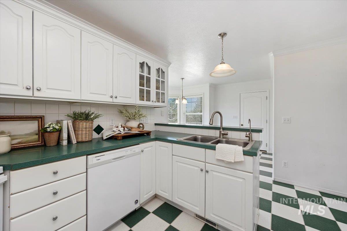 Kitchen with light flooring, white dishwasher, white cabinets, tasteful backsplash, and crown molding