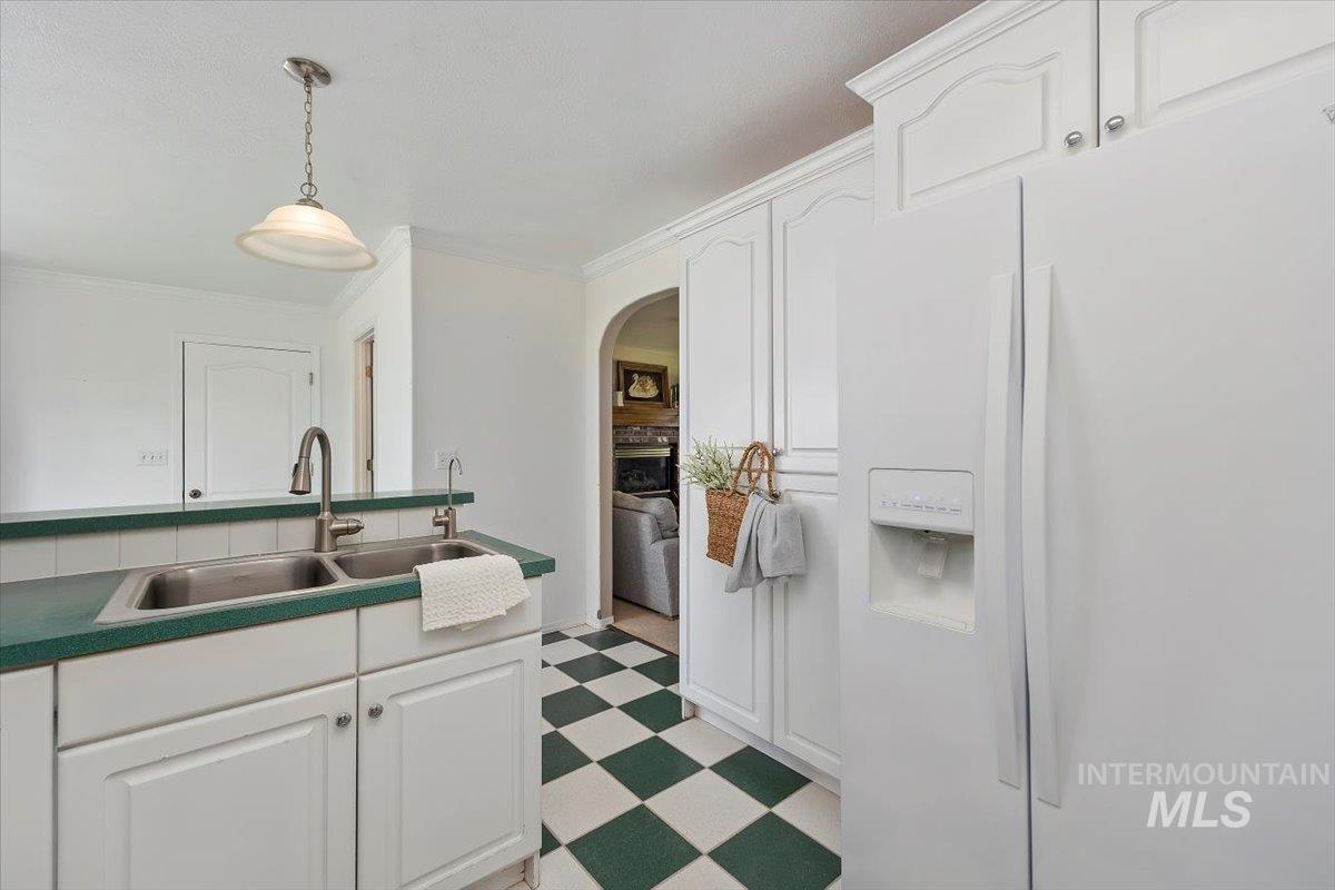 Kitchen with white fridge with ice dispenser, white cabinets, pendant lighting, light floors, and crown molding
