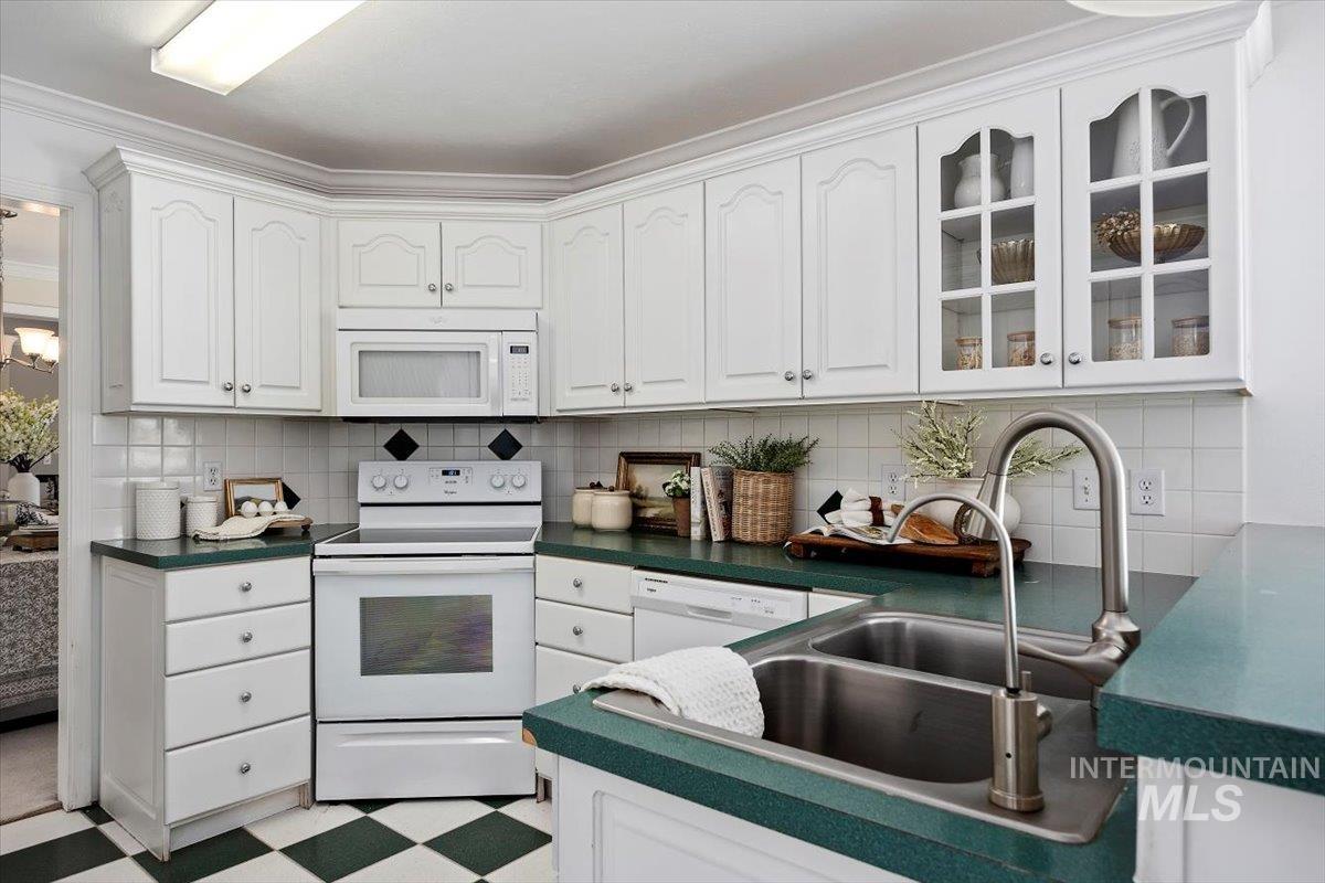 Kitchen featuring white appliances, dark countertops, white cabinets, decorative backsplash, and crown molding
