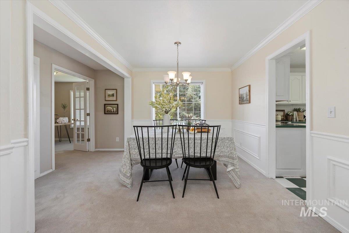 Dining room featuring light carpet, a chandelier, ornamental molding, a decorative wall, and wainscoting
